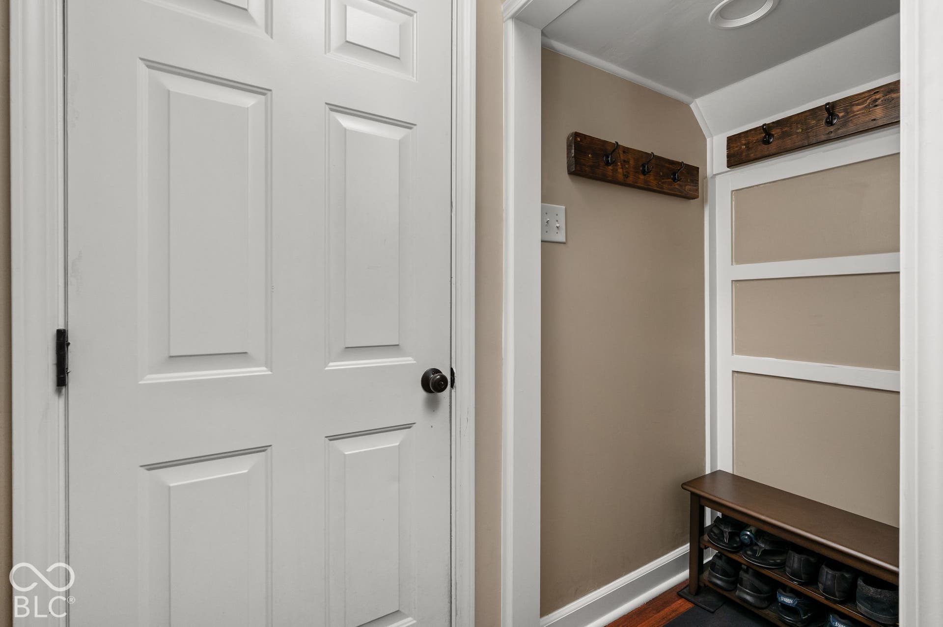 Panel door with dark hardware, recessed lighting, and a built-in storage bench with shelving