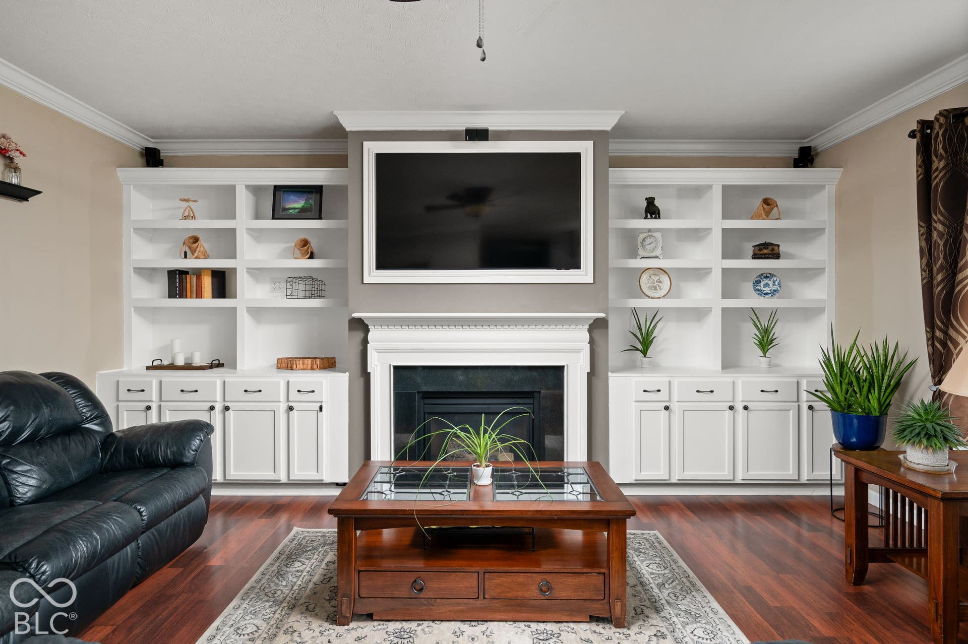 Built-in cabinetry flanking a central fireplace with a decorative mantel, crown molding, and wood-finish flooring