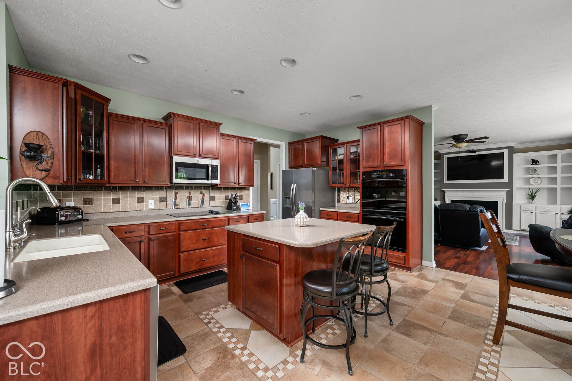 Kitchen featuring wood cabinetry, light-toned countertops, a tile backsplash, stainless steel appliances, and a central island with seating