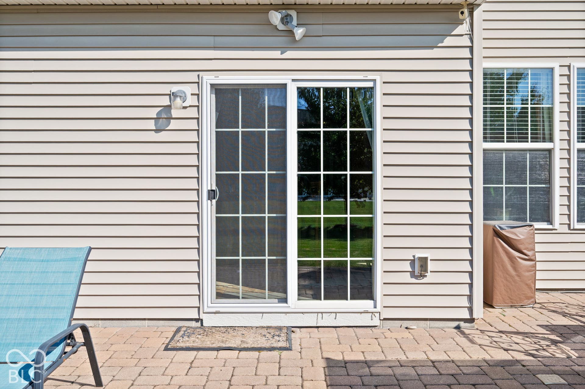 Patio with brick paver hardscaping, sliding glass door with grids, and horizontal siding