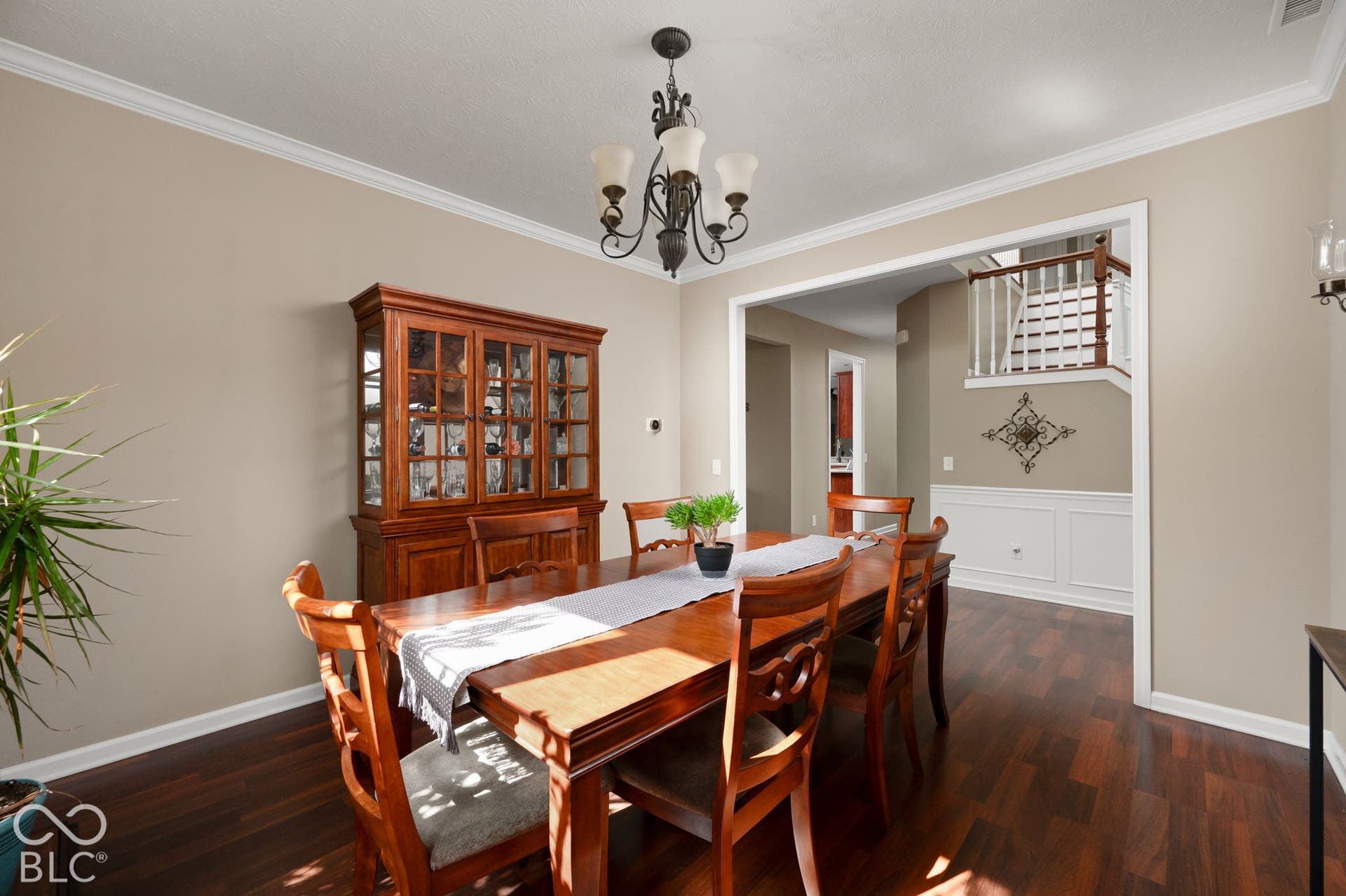 Dark wood-finish flooring, crown molding, and a chandelier illuminate the dining space