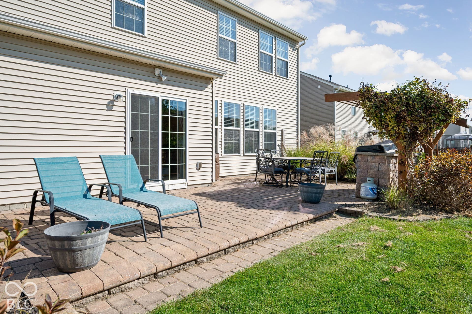 Paved patio area, sliding glass door access, exterior siding, and a partial pergola structure