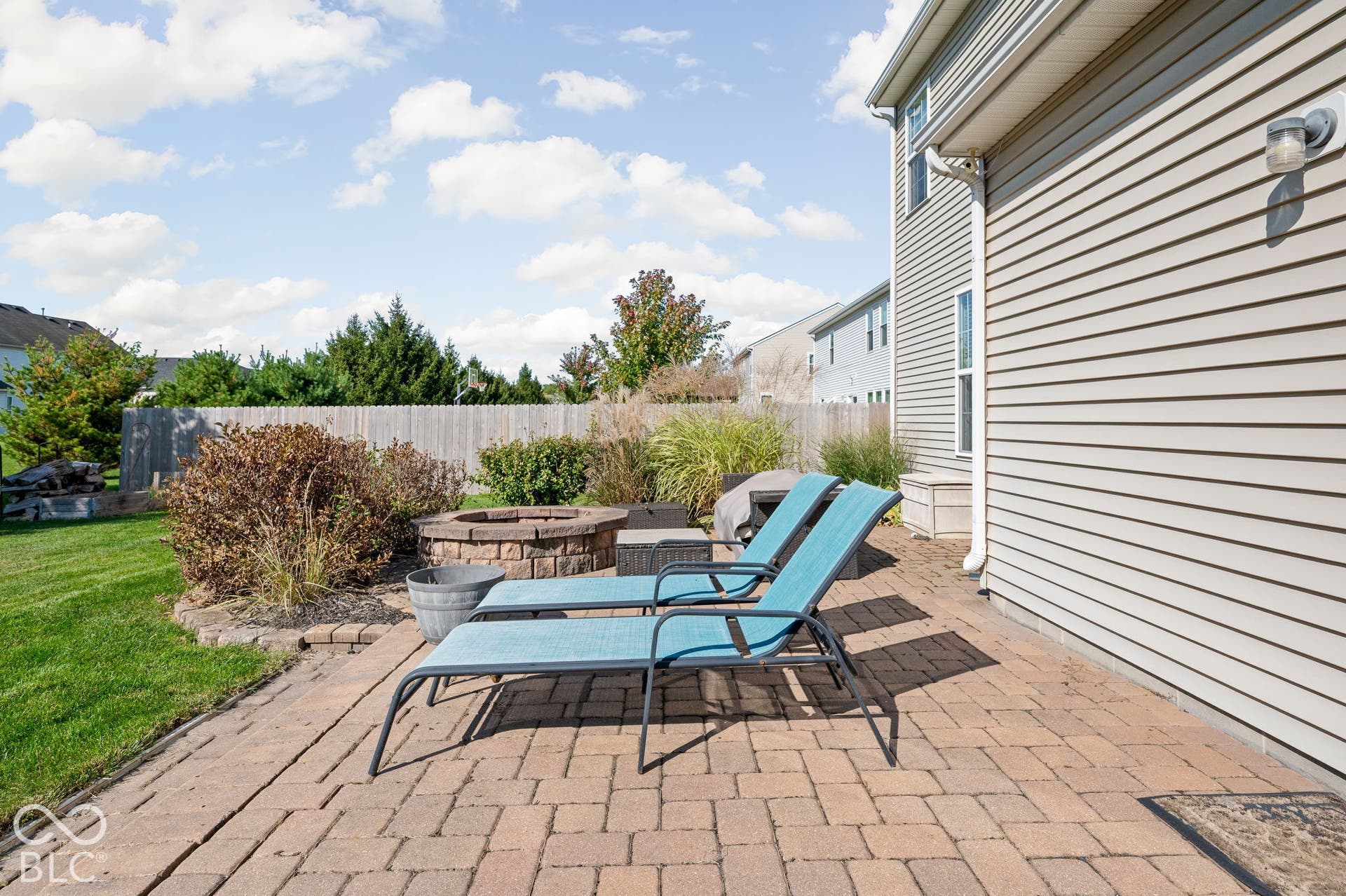 Expansive paver patio with a built-in stone fire pit, bordered by a manicured lawn and mature shrubs