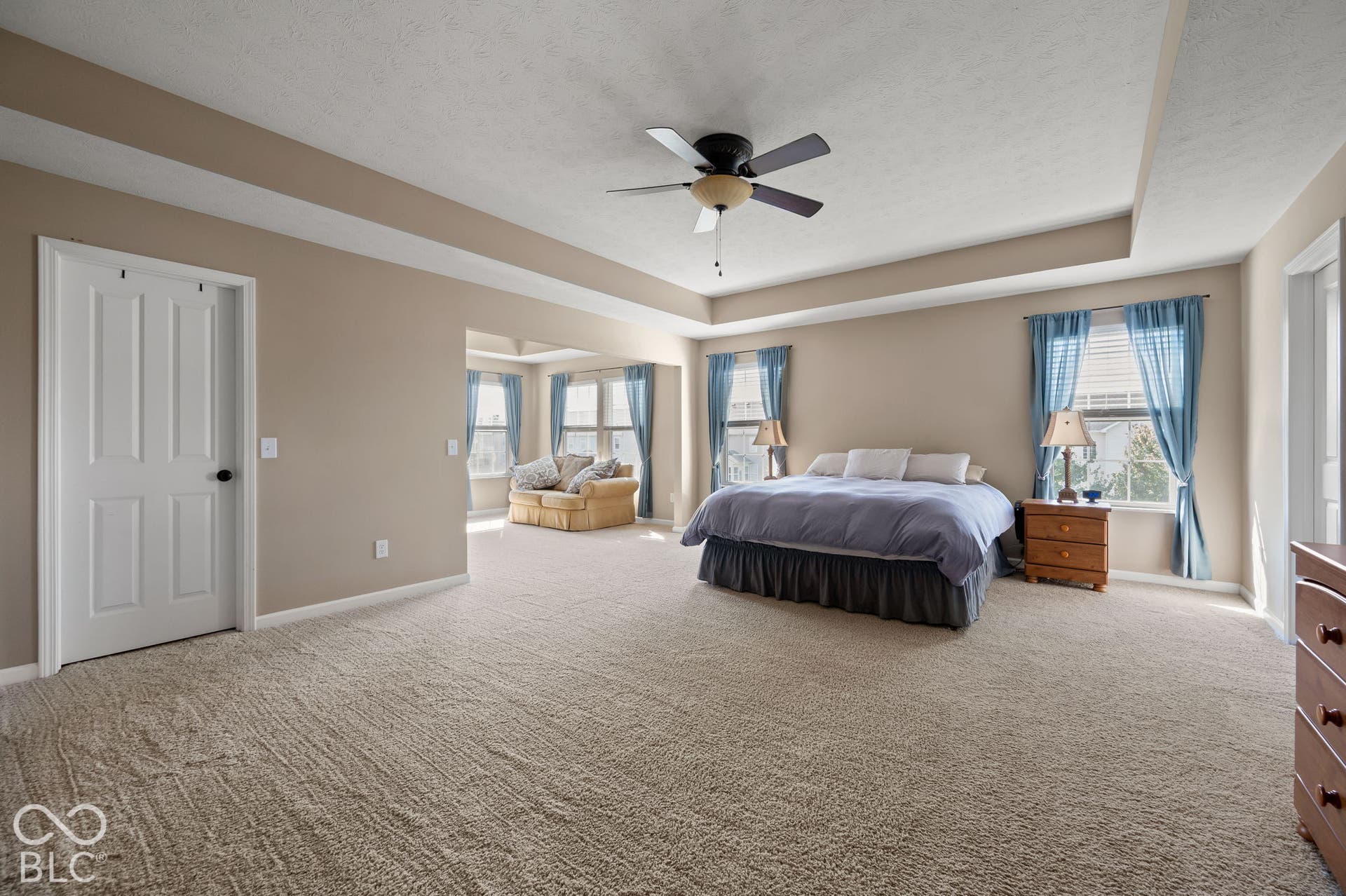 Tray ceiling with a ceiling fan, neutral wall paint, and light-toned carpeting throughout
