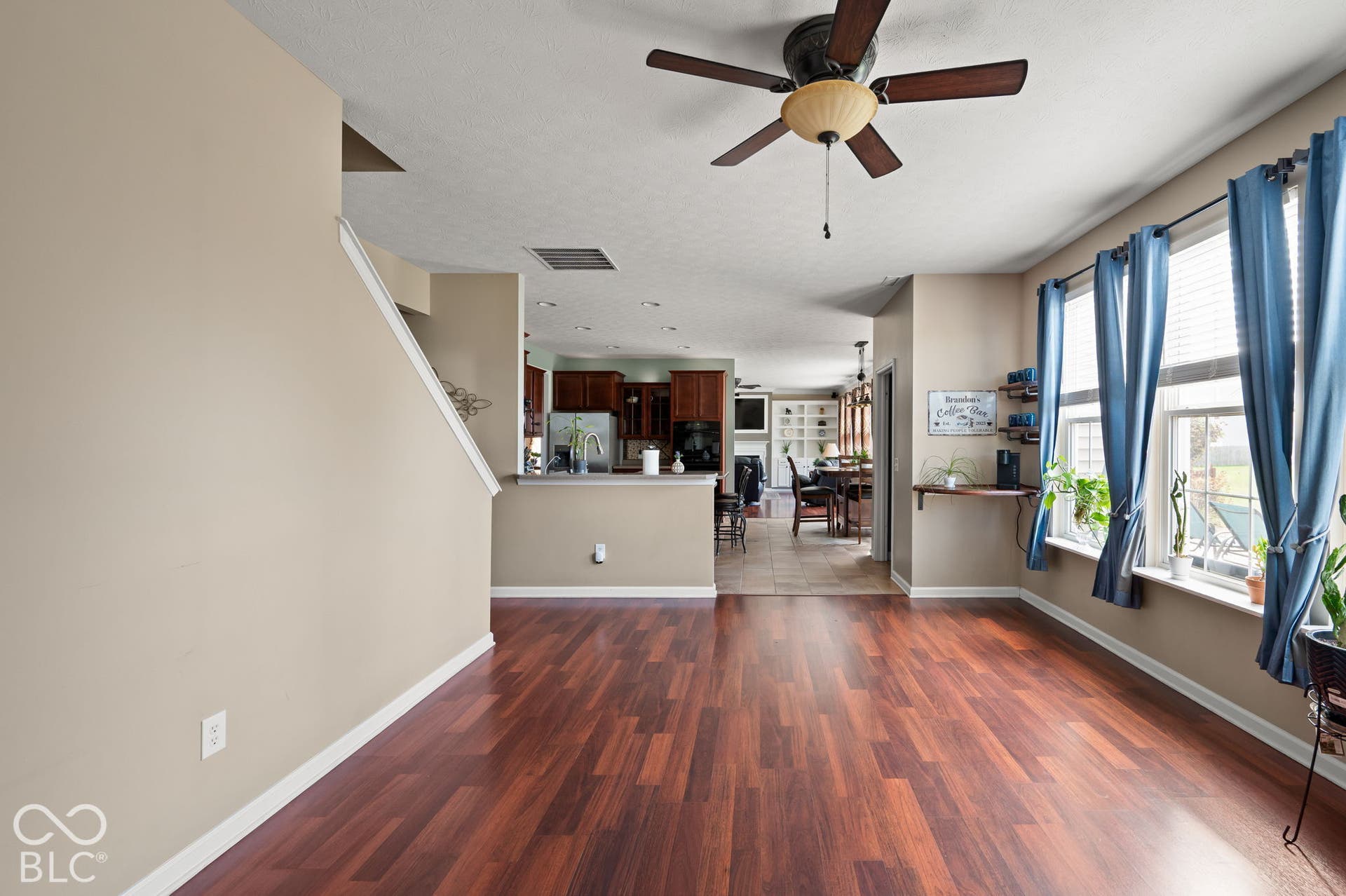Wood-finish flooring throughout, ceiling fan with integrated lighting, and multiple windows with blinds