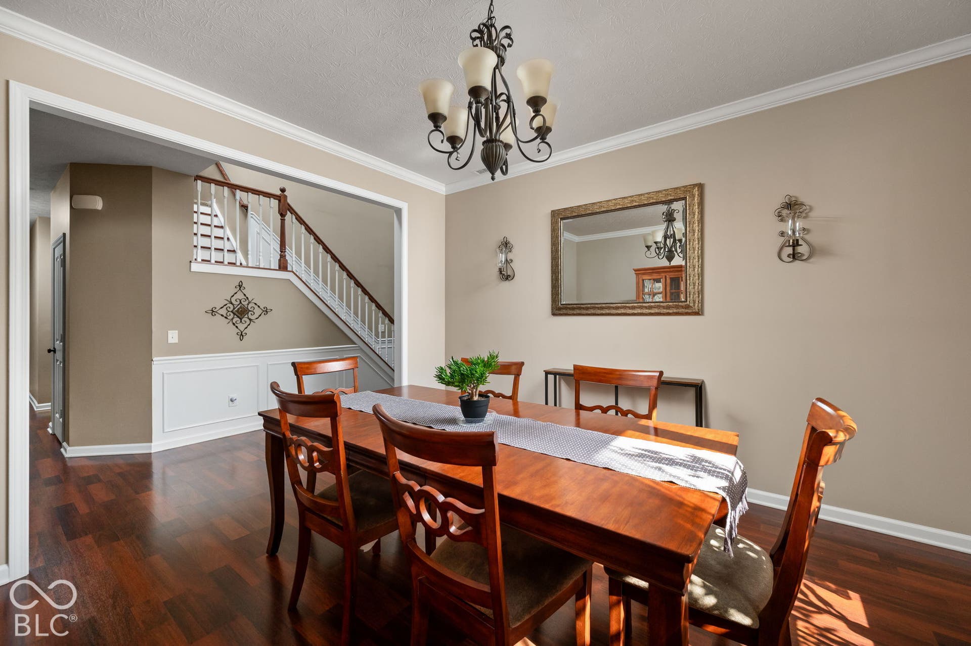 Hardwood-finish flooring, crown molding, wainscoting, decorative wall sconces, and a chandelier with glass shades