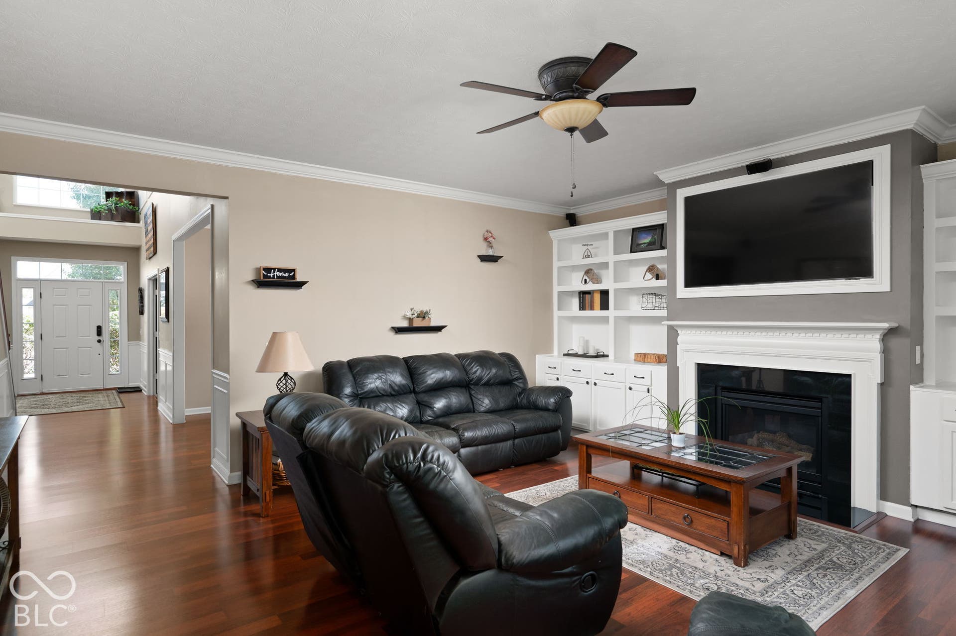 Hardwood flooring, crown molding, built-in shelving, a fireplace with mantel, and a ceiling fan