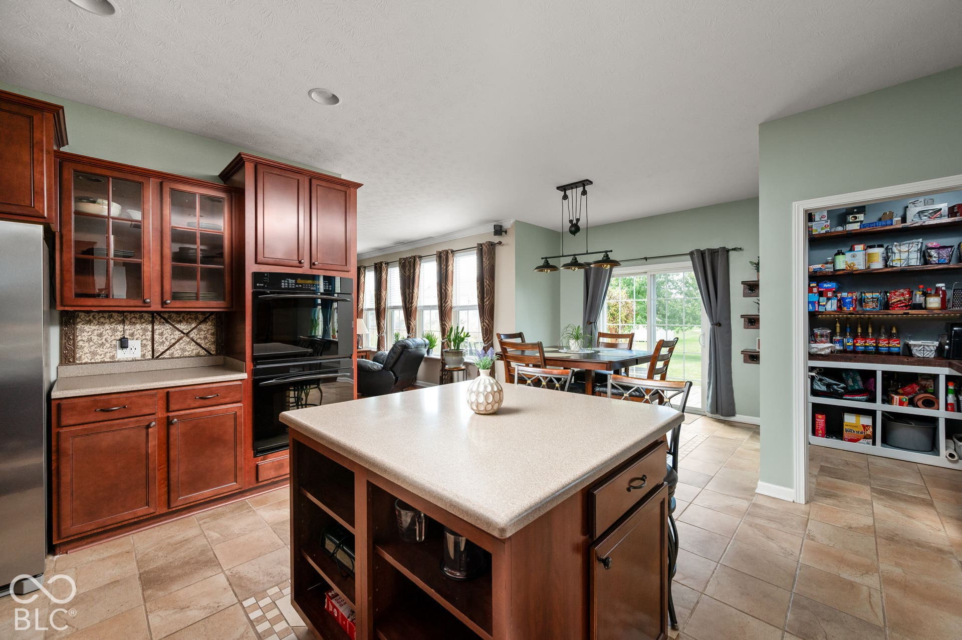 Kitchen featuring wood cabinetry, built-in double ovens, a center island with countertop, and tile flooring