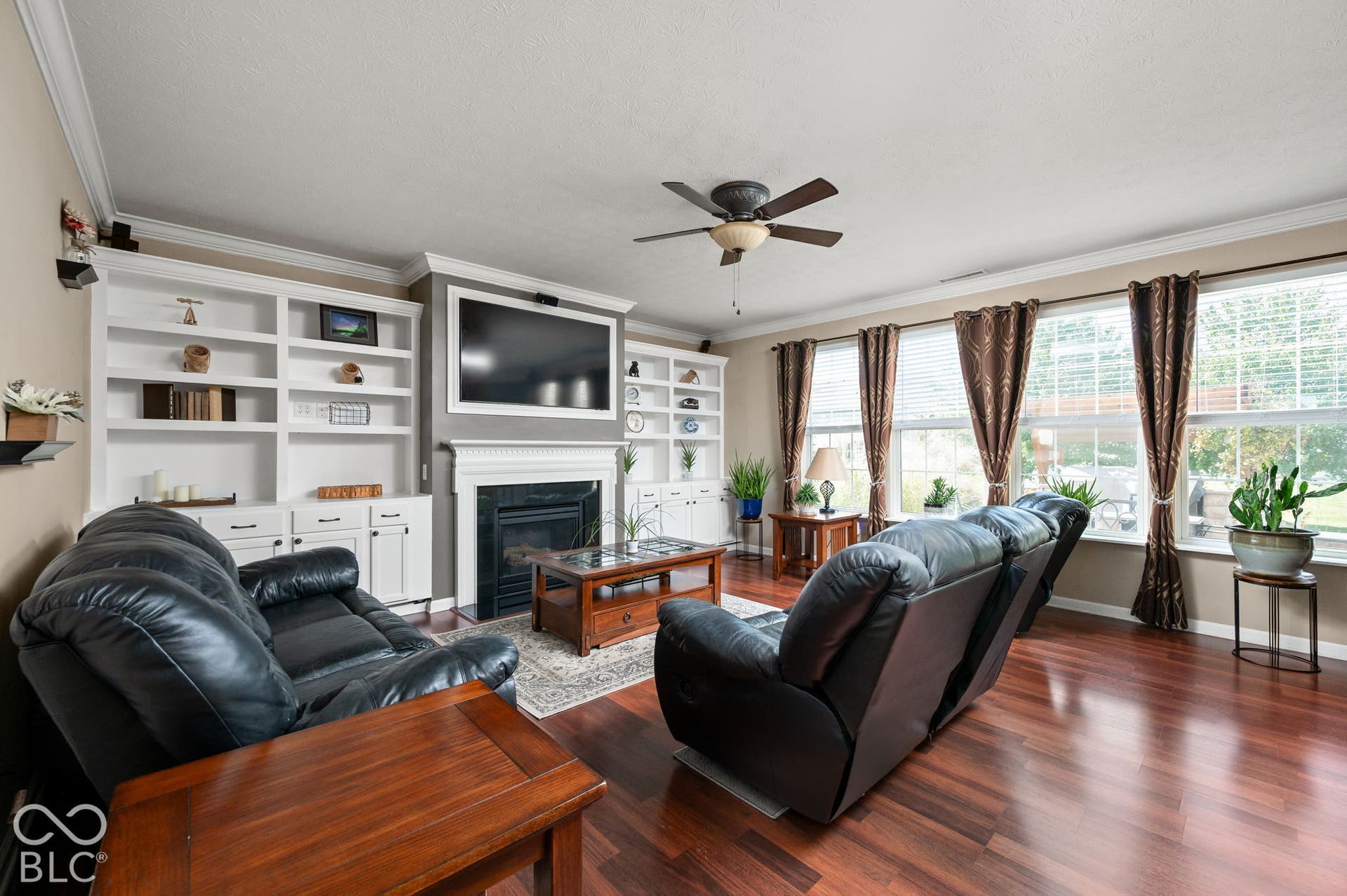 Wood-finish flooring throughout, integrated ceiling fan with lighting, built-in shelving, and a fireplace with mantle