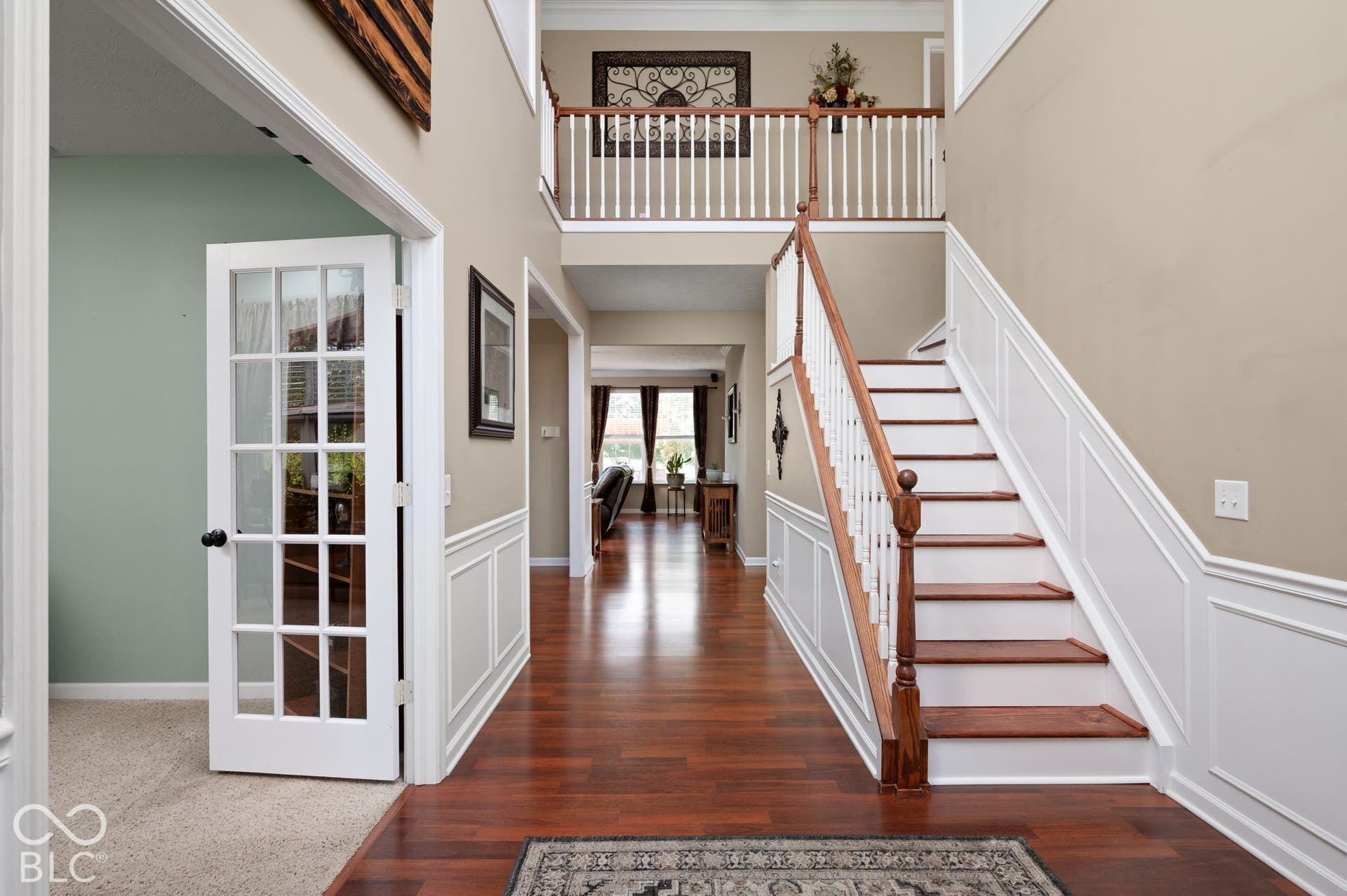 Two-story foyer with wood-finish flooring, wainscoting, and a staircase featuring wood newel posts and railings
