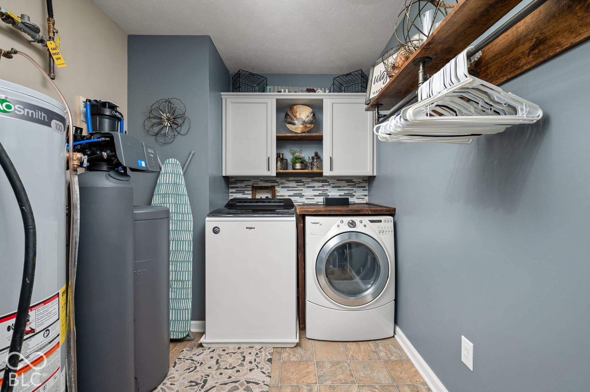 Upstairs Laundry area featuring a built-in water heater, water treatment system, wood-finish countertop, upper cabinetry, and a tile backsplash