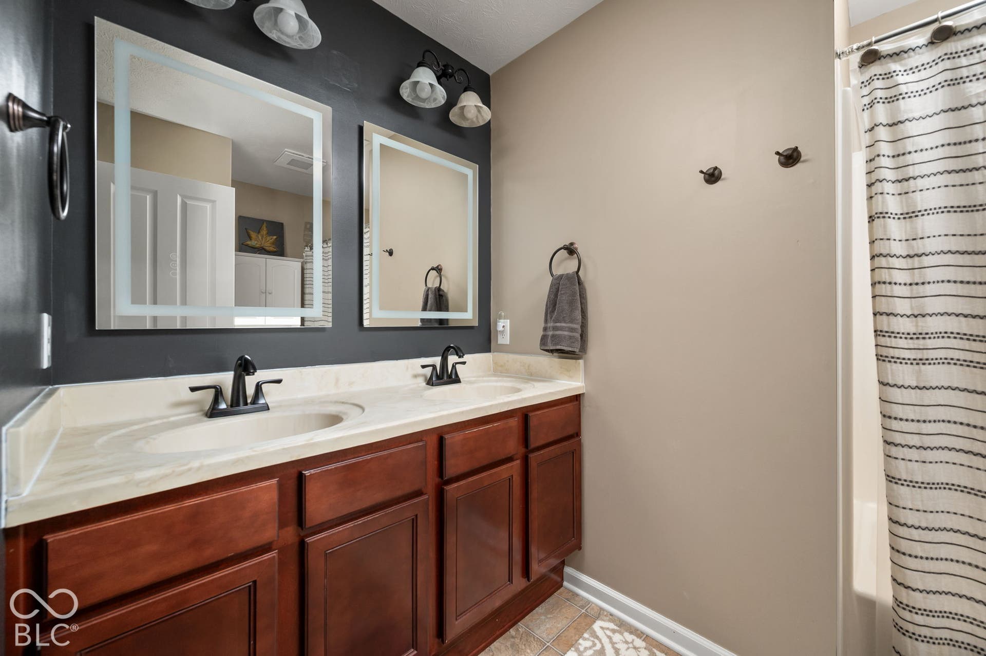 Dual vanity with integrated sinks, wood-finish cabinetry, and contemporary illuminated mirrors
