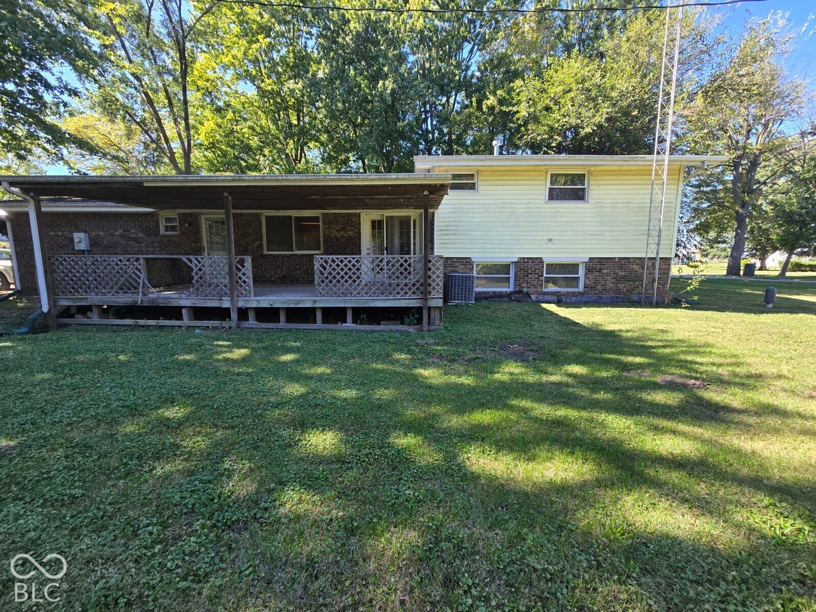 Rear exterior featuring a covered deck with lattice railing, brick lower facade, and light-colored siding