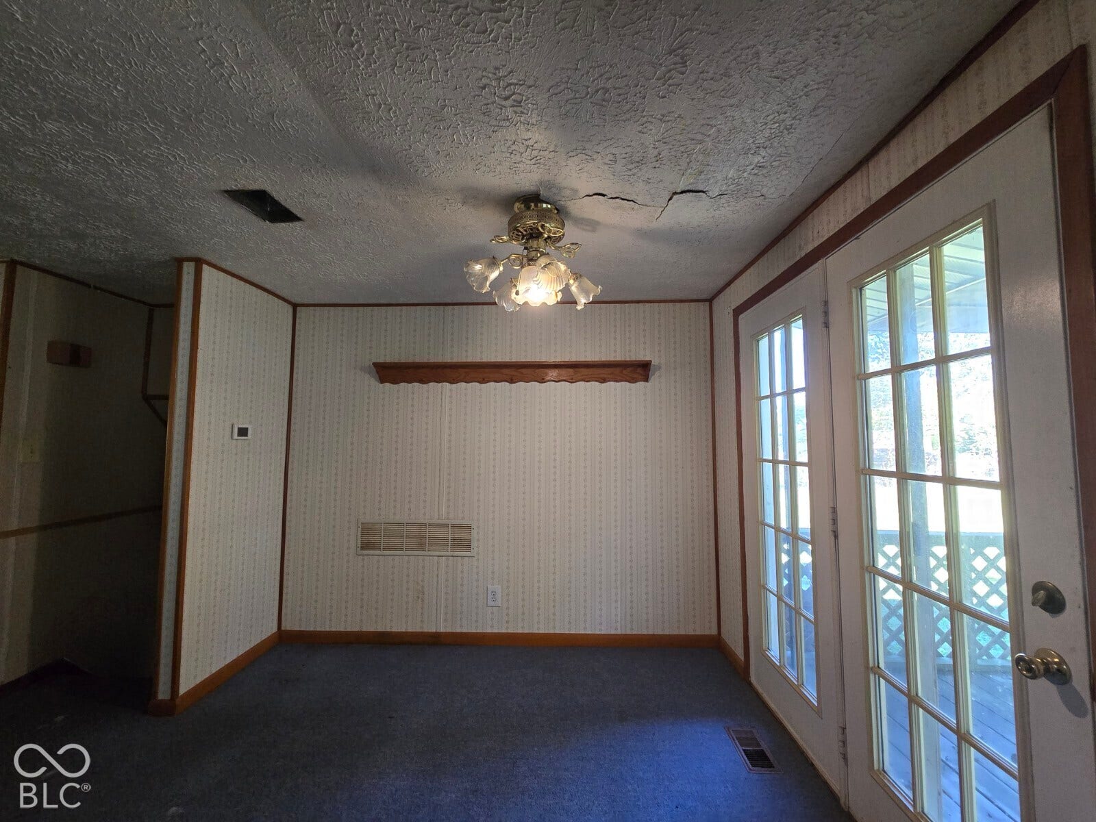 Double French doors with exterior lattice details, ceiling-mounted light fixture, wood trim, and wall-mounted shelving