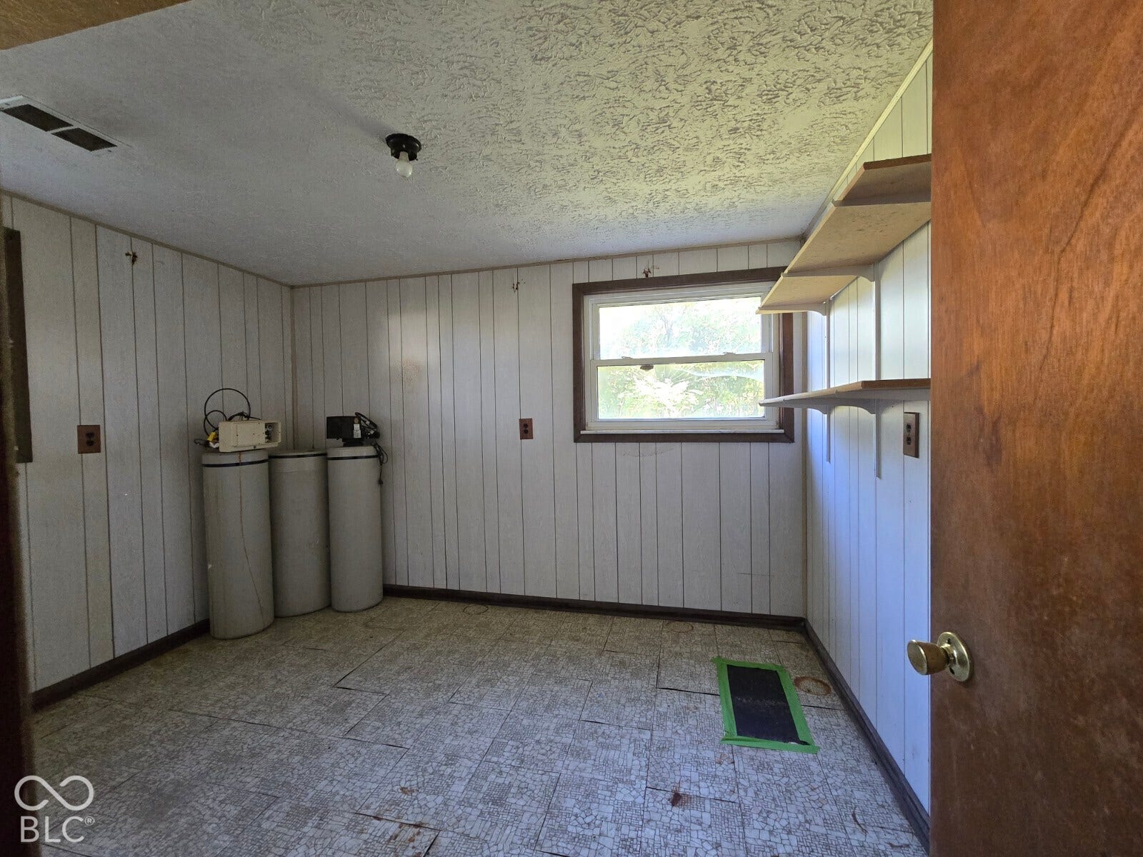 Wall-mounted shelving units, an operational single-pane window, and vinyl plank flooring