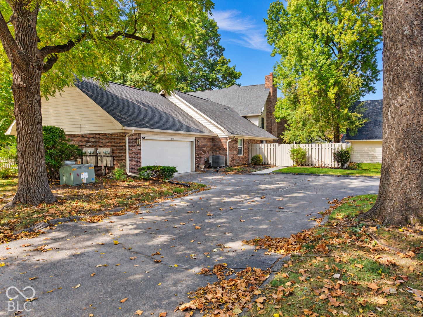 Charming brick and siding residence featuring a two-car garage, circular driveway with stone paving, and mature shade trees framing the property