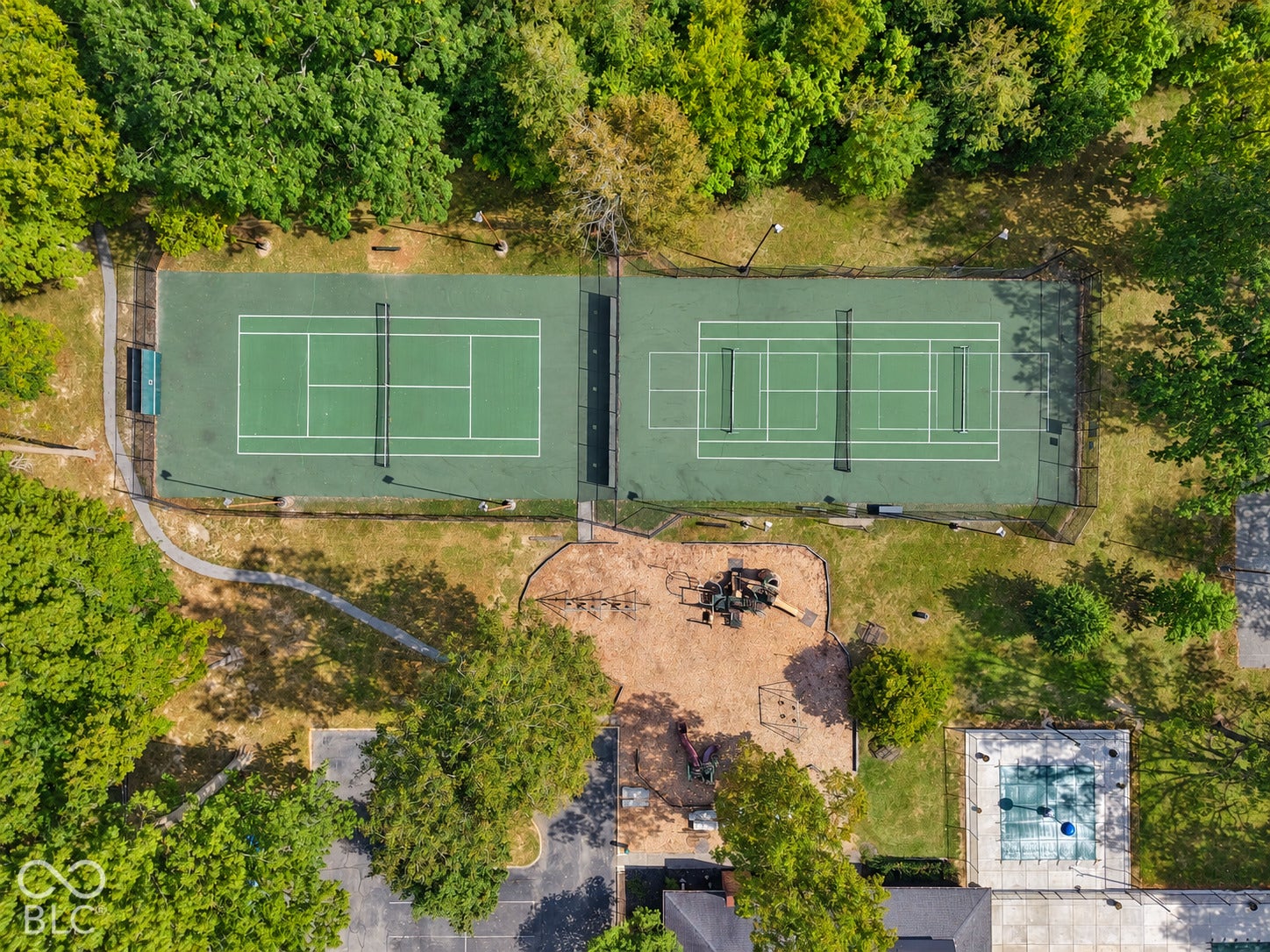 Dual professional-grade tennis courts with meticulously maintained hard courts and regulation net systems, surrounded by mature landscaping and lush tree canopy