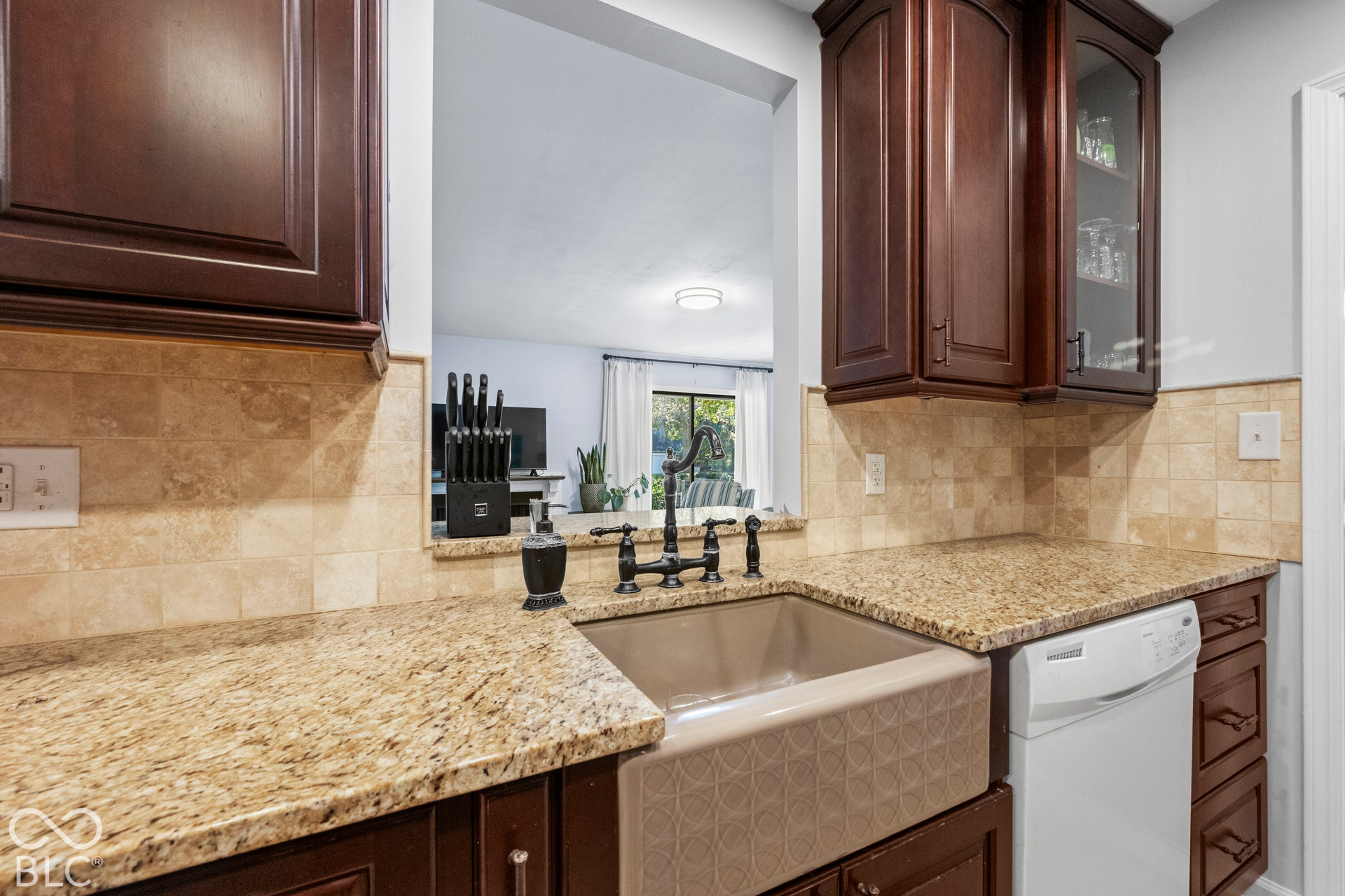 Rich wood cabinetry, granite countertops, tile backsplash, farmhouse-style sink, and integrated dishwasher