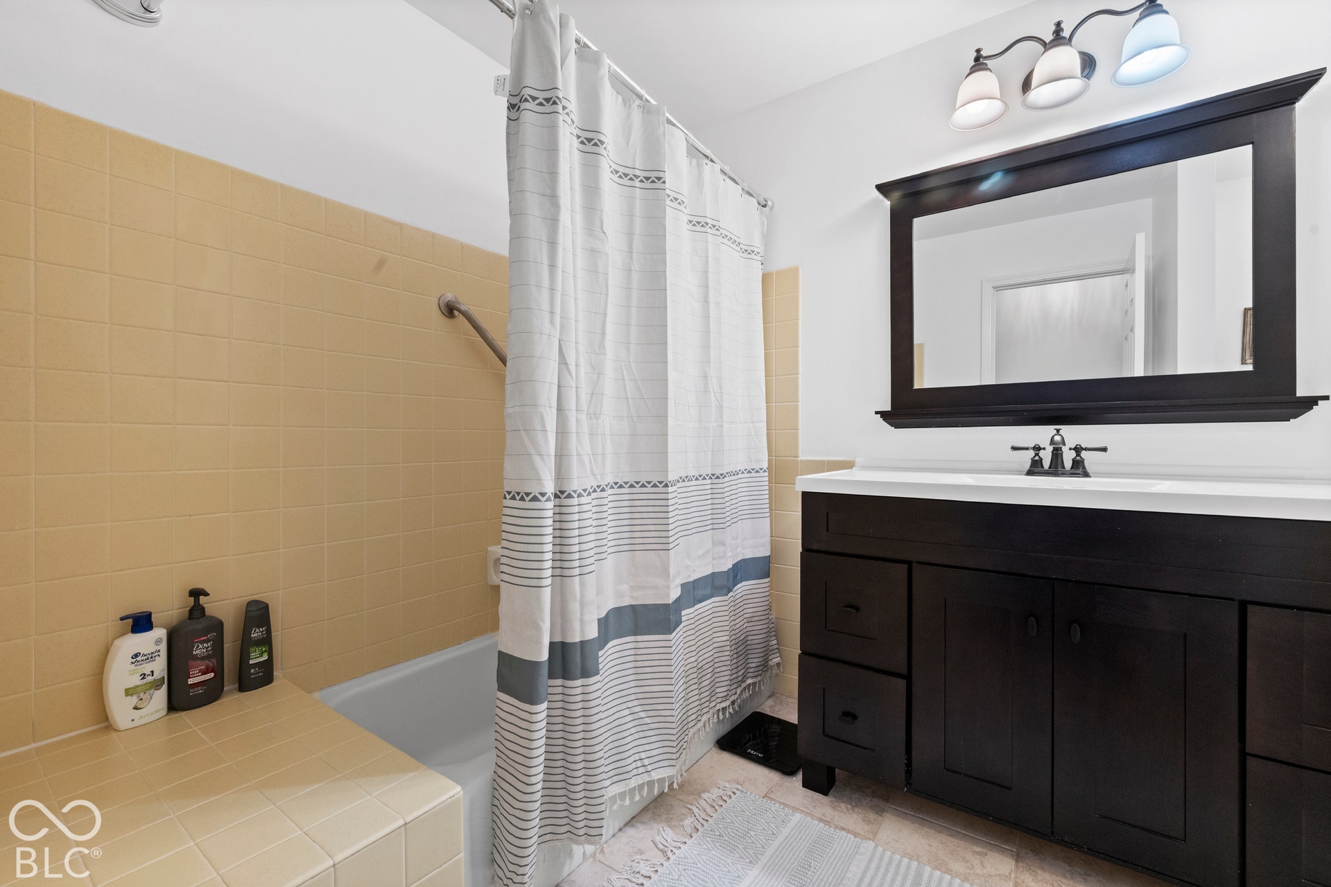 Bathroom featuring a dark wood finish vanity with integrated sink, rectangular framed mirror, and a three-light vanity fixture