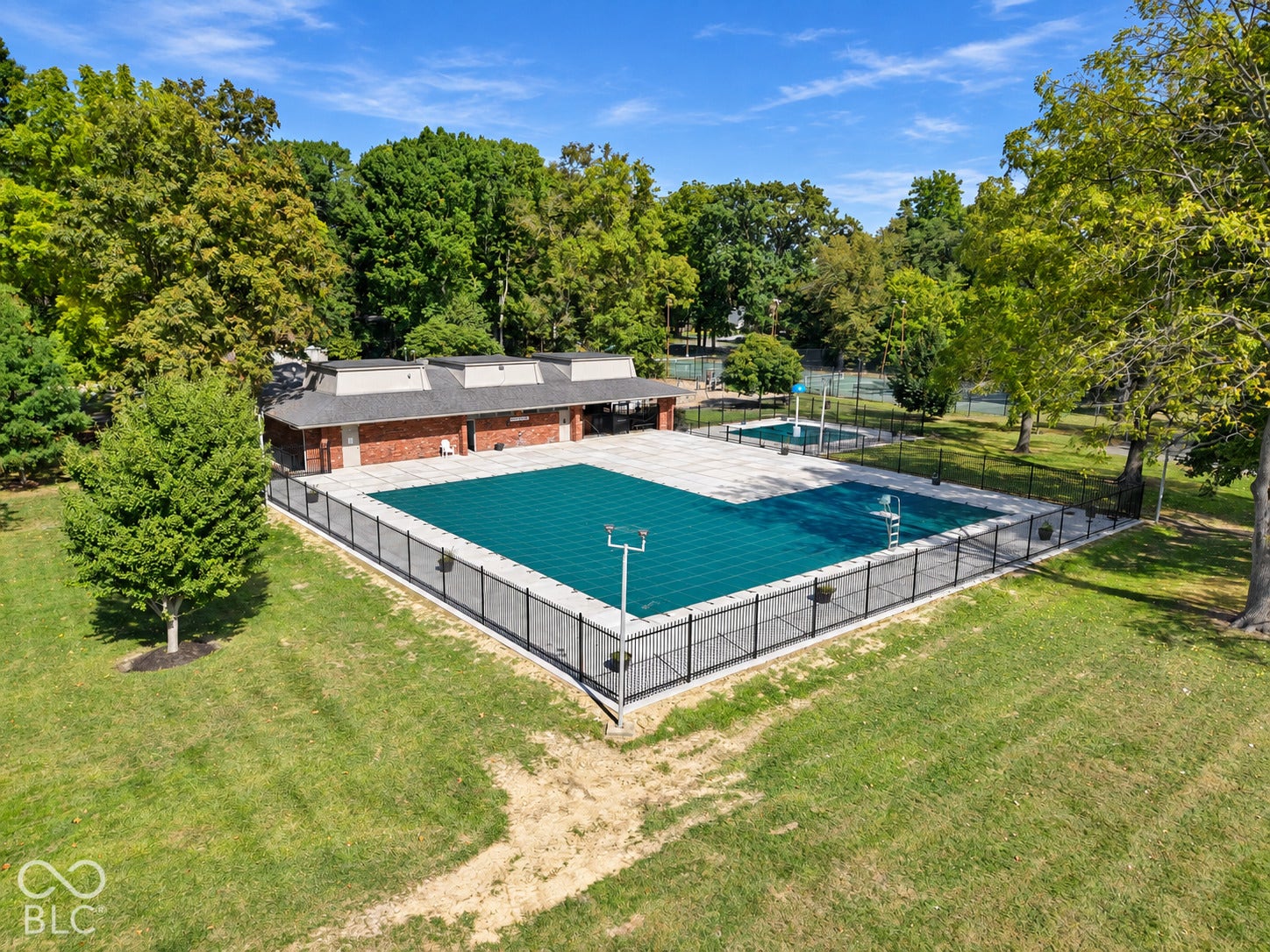 Expansive swimming pool area with a secure perimeter fence, surrounding concrete decking, and a red brick pool house