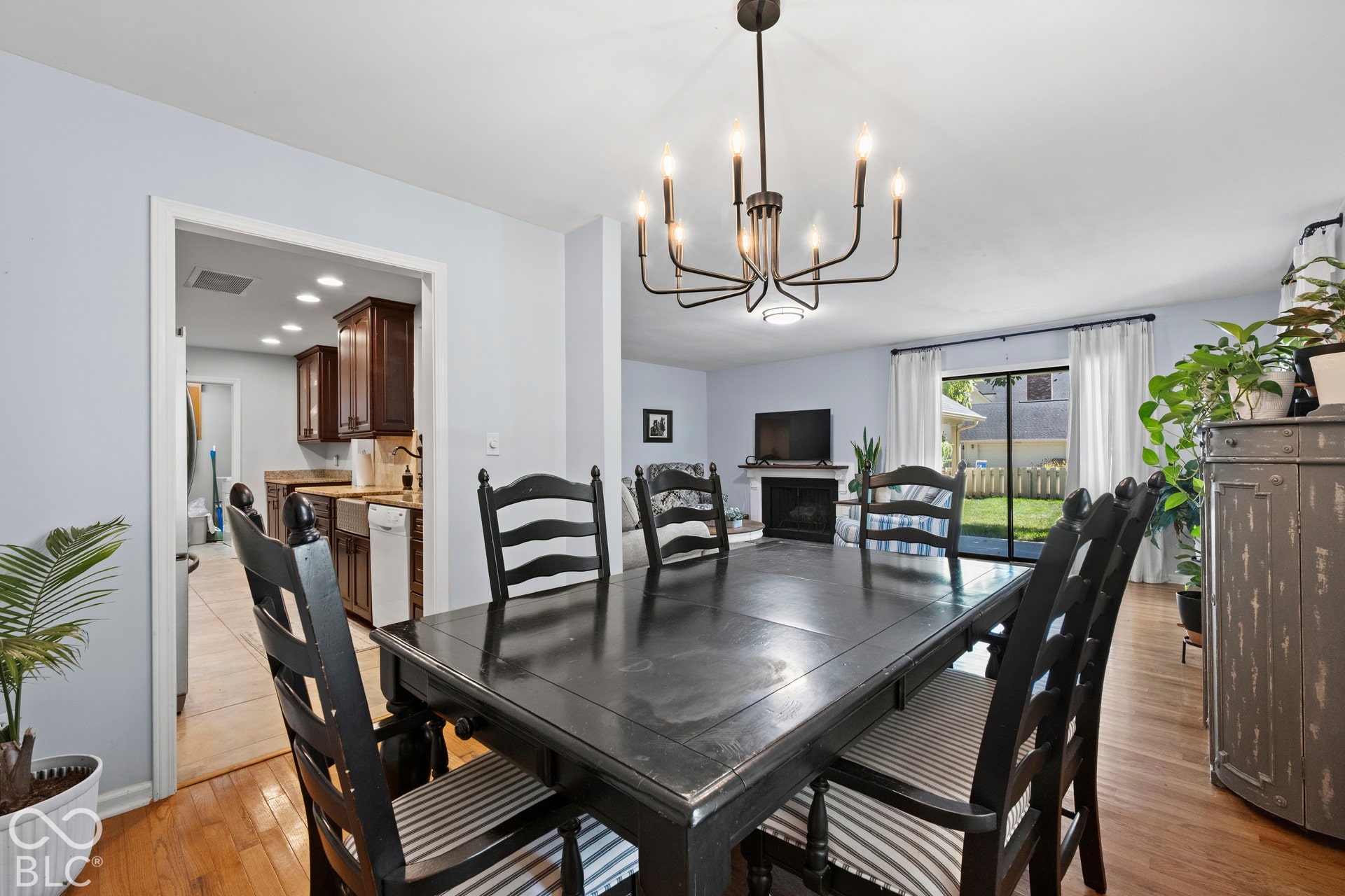 Hardwood flooring, recessed lighting, and a modern chandelier illuminate the dining area, with a fireplace and sliding glass door to the rear yard