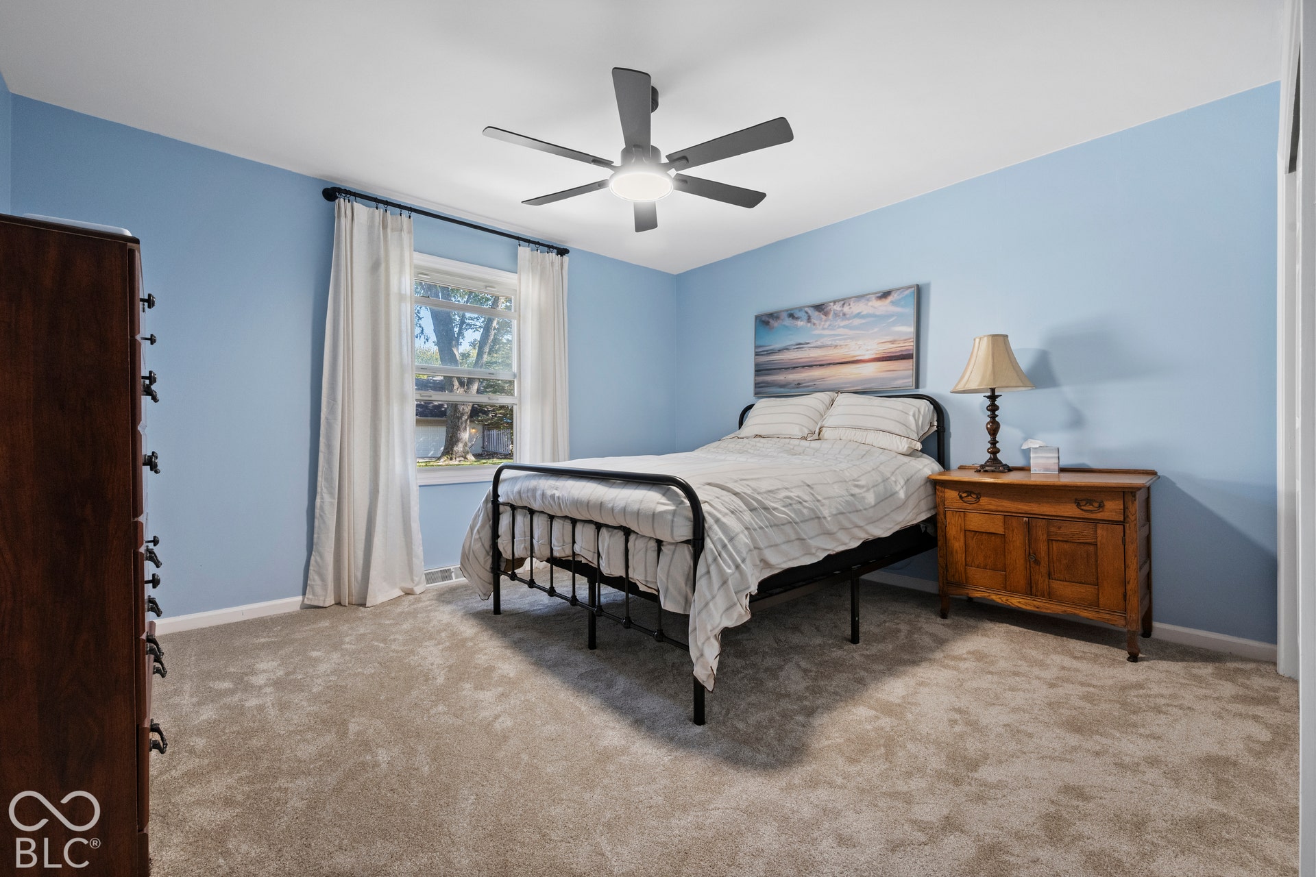 Window with white trim and drapery rod, ceiling fan with integrated lighting, light-colored carpeting, blue-painted walls