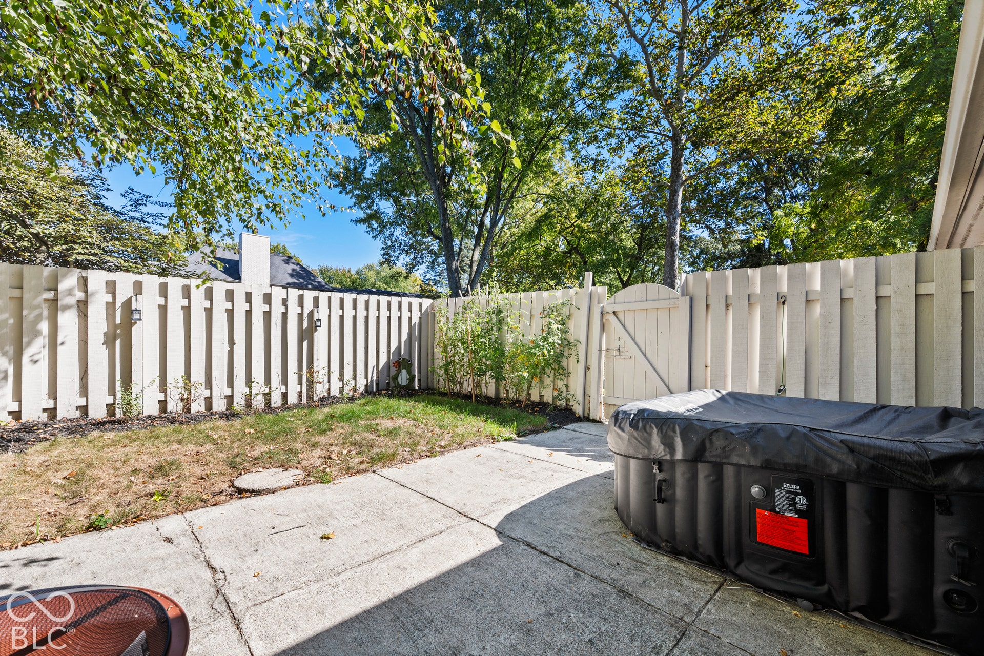 Fenced backyard with white vinyl privacy fencing, concrete patio, and mature shade trees providing natural canopy coverage