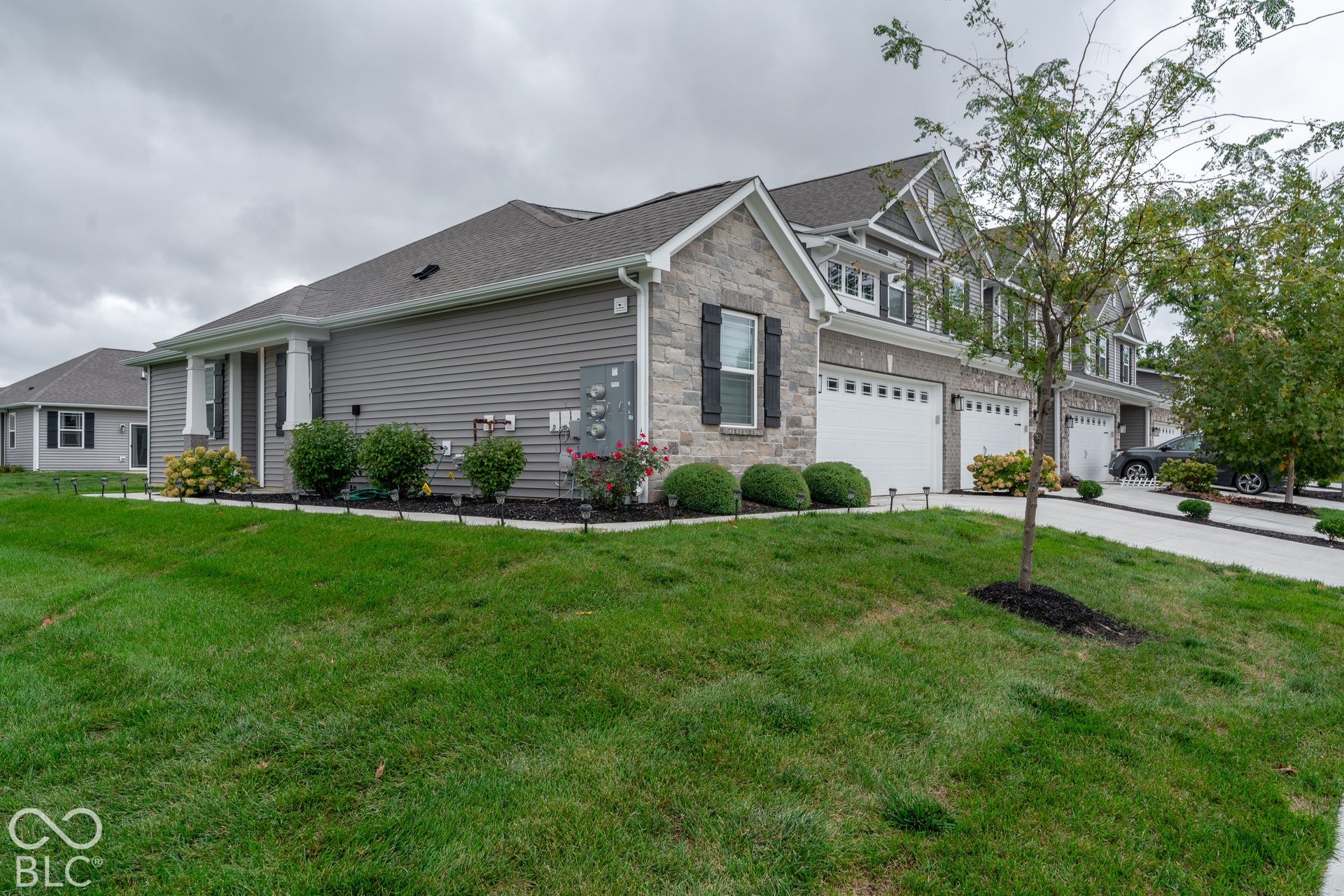6432 Yuma, Whitestown, IN 46075 Stone and siding exterior with dark shutters, multiple garage doors, and landscaped beds featuring shrubs and flowering plants