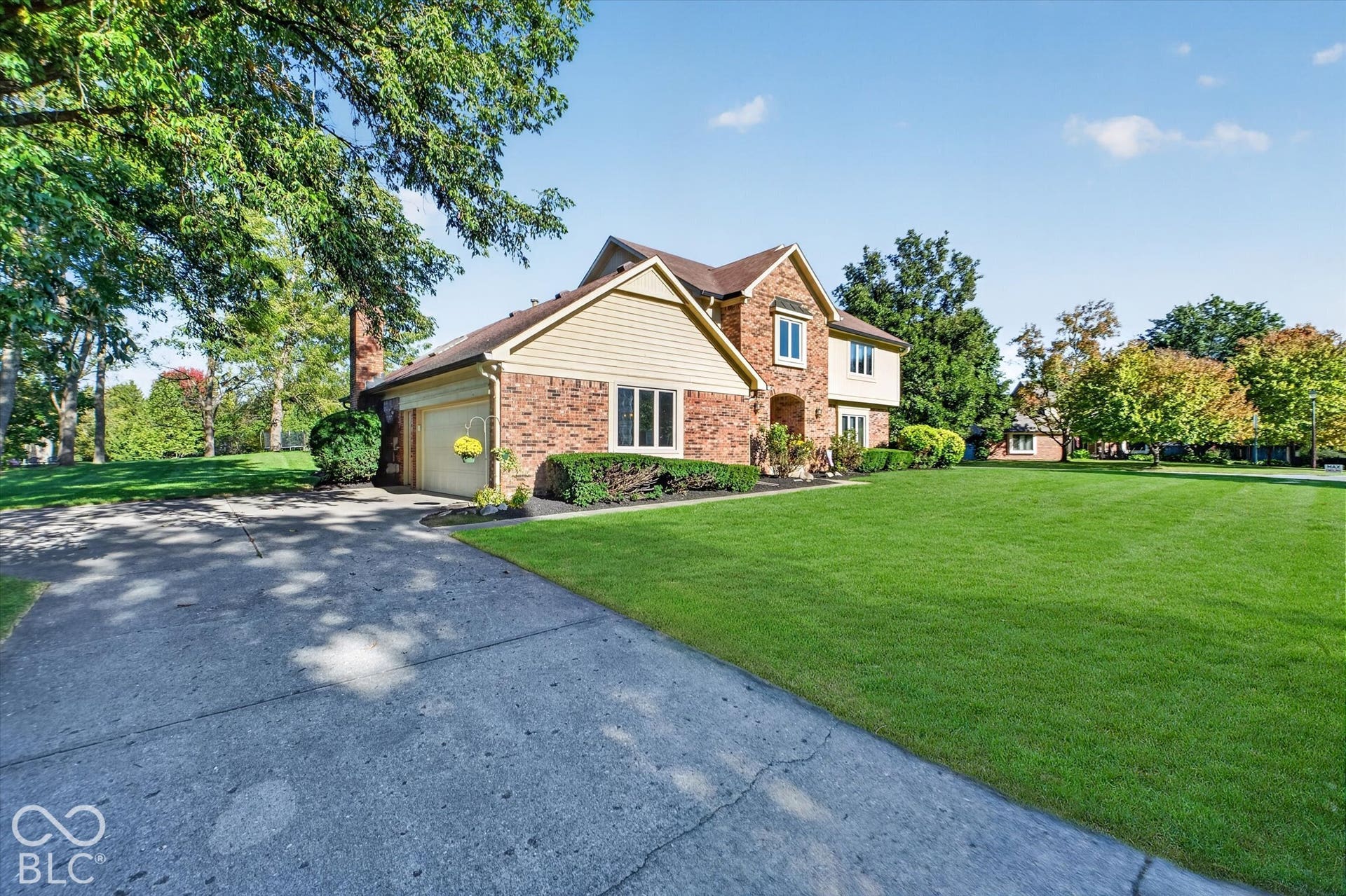 Brick and siding exterior with a concrete driveway, attached garage, and mature trees