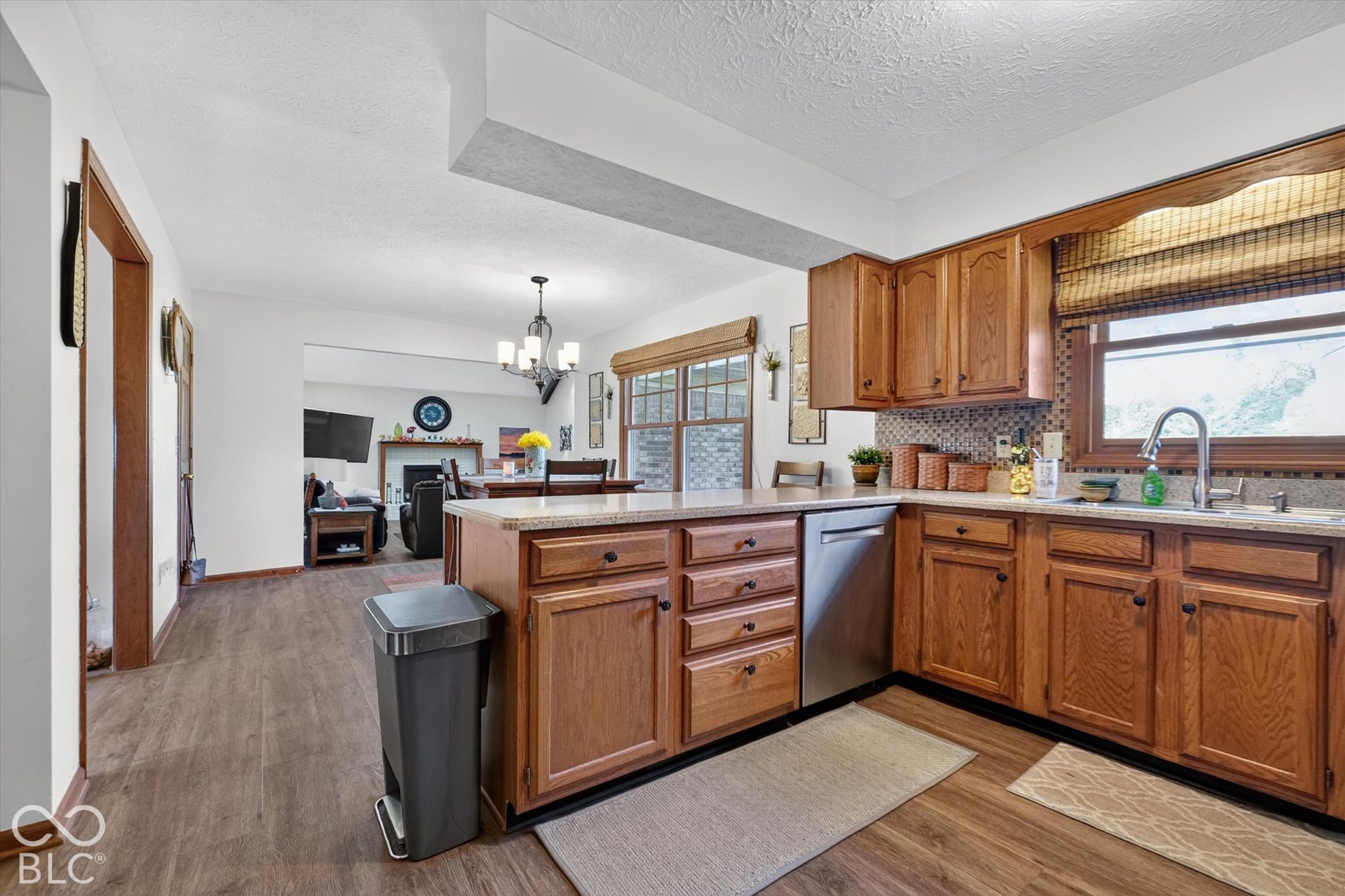 Wood-finish flooring throughout, kitchen island with integrated cabinetry, stainless steel dishwasher, wood cabinetry, and a tile backsplash