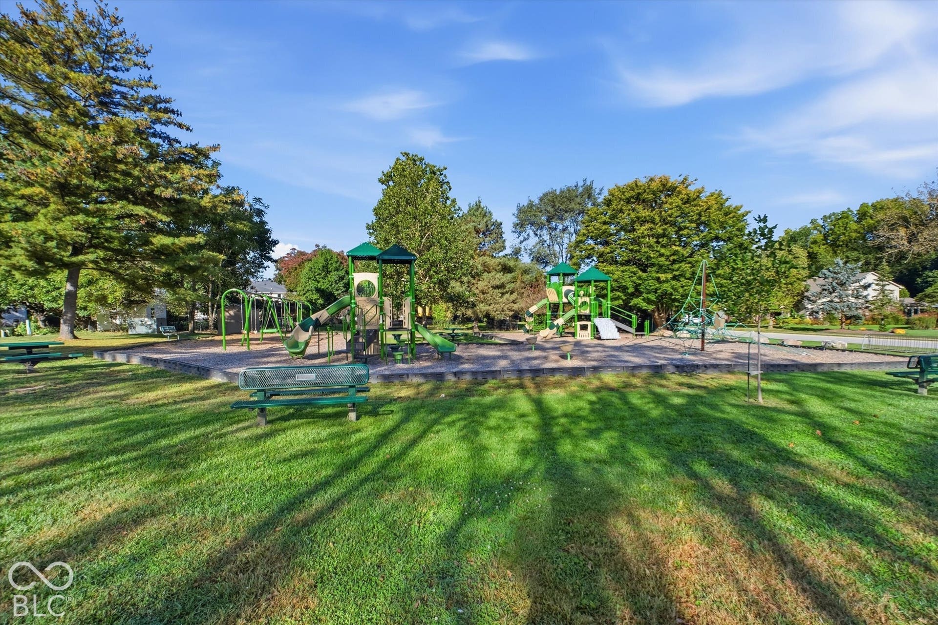 Expansive green space featuring a dedicated playground area, mature trees, and picnic benches