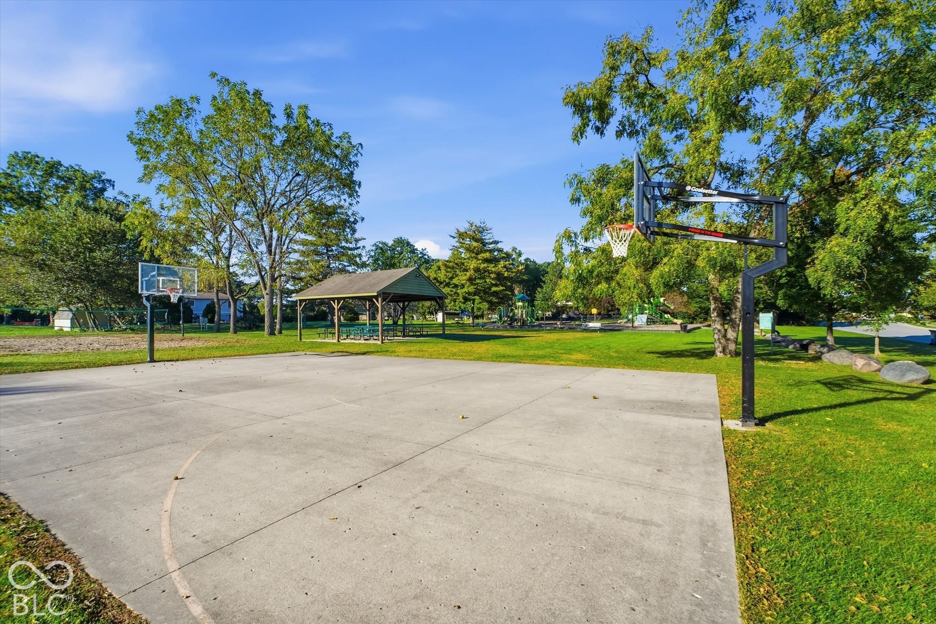 Basketball court with two hoops, concrete surface, and surrounding green space