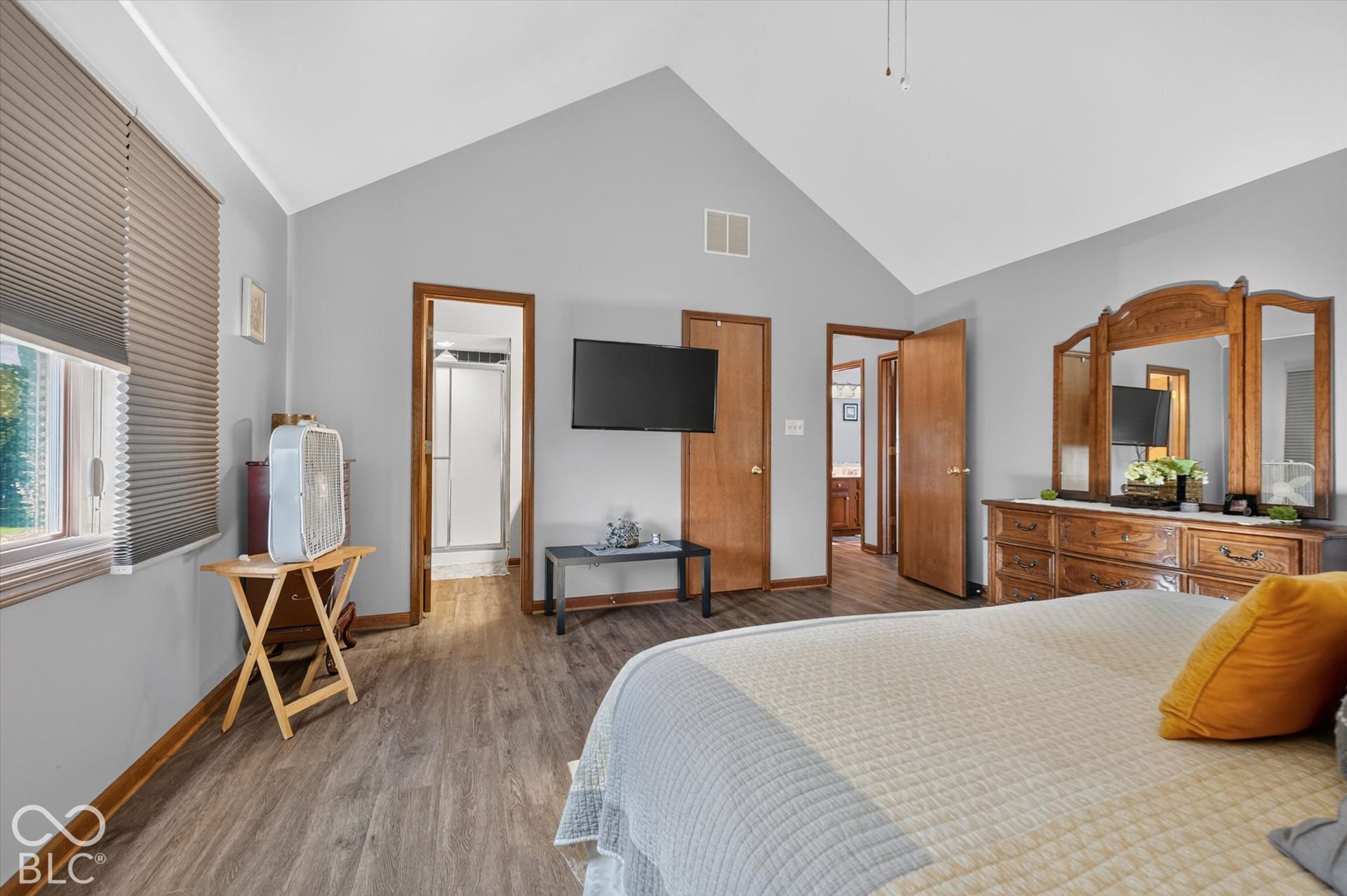 Vaulted ceiling, wood-finish flooring, light grey wall paint, white trim, and a window with blinds