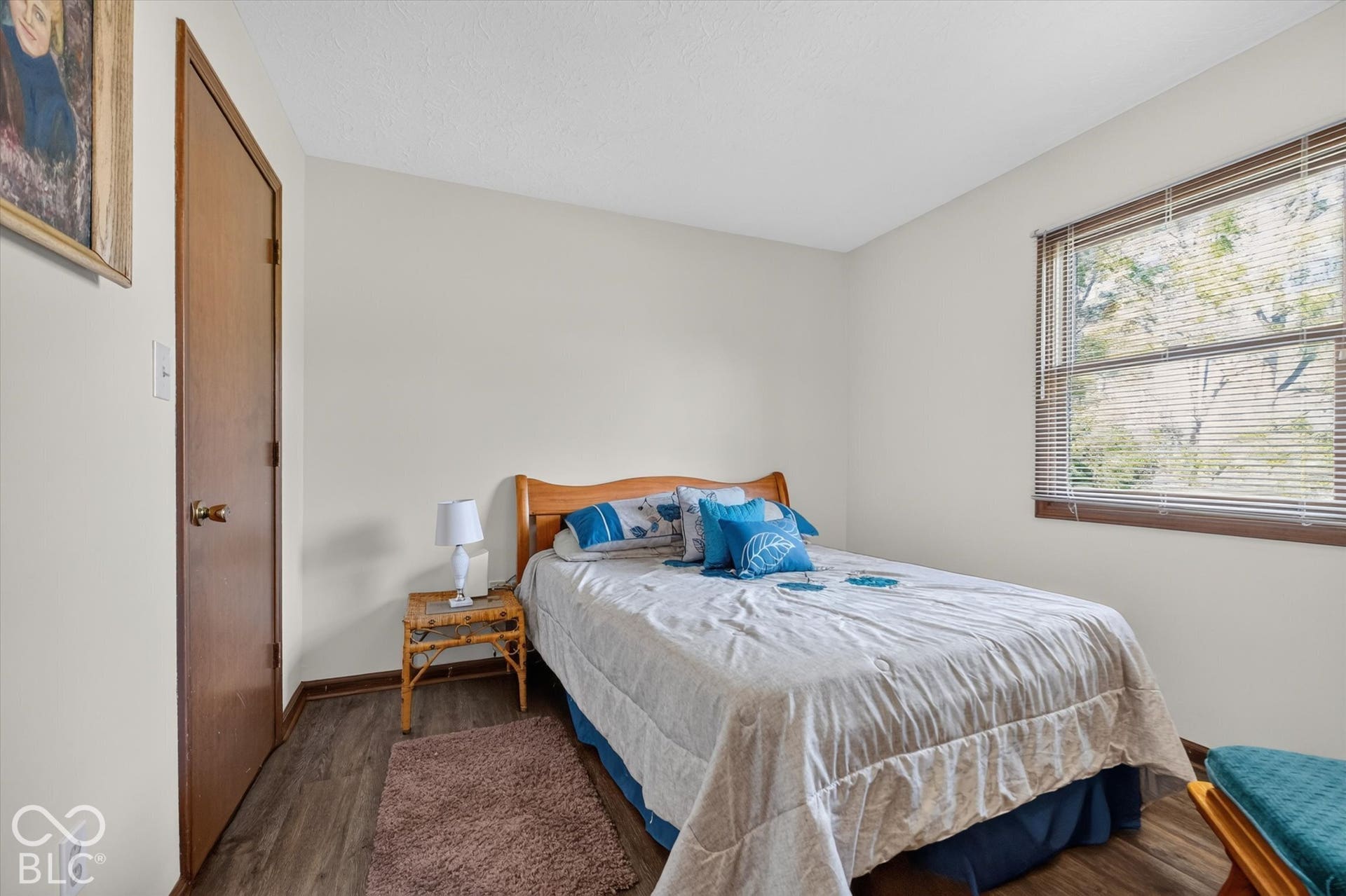 Wood-finish flooring with a wood door, white walls, and a window with blinds