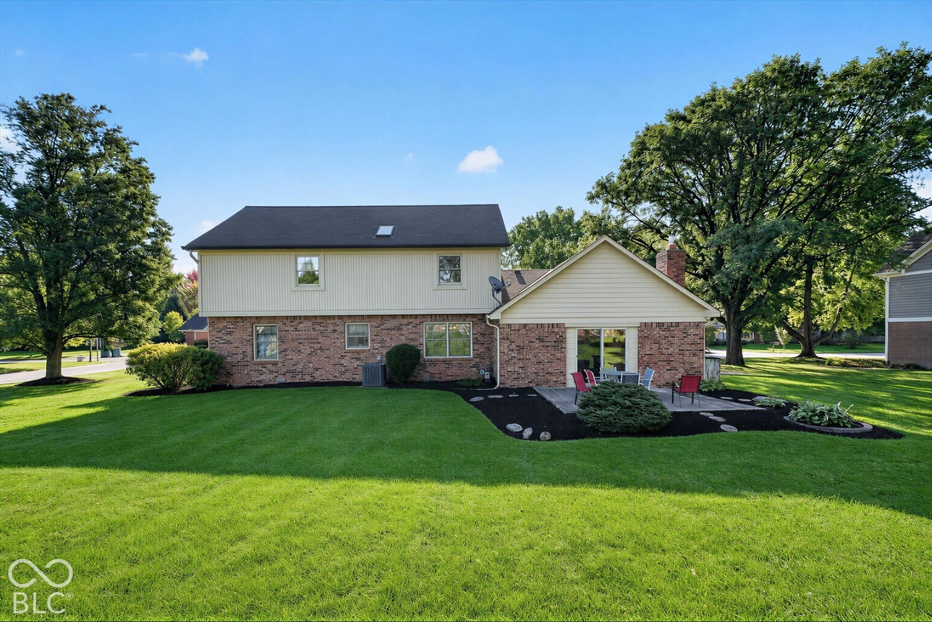 Expansive lawn with mature trees, brick and siding exterior, and a stone patio