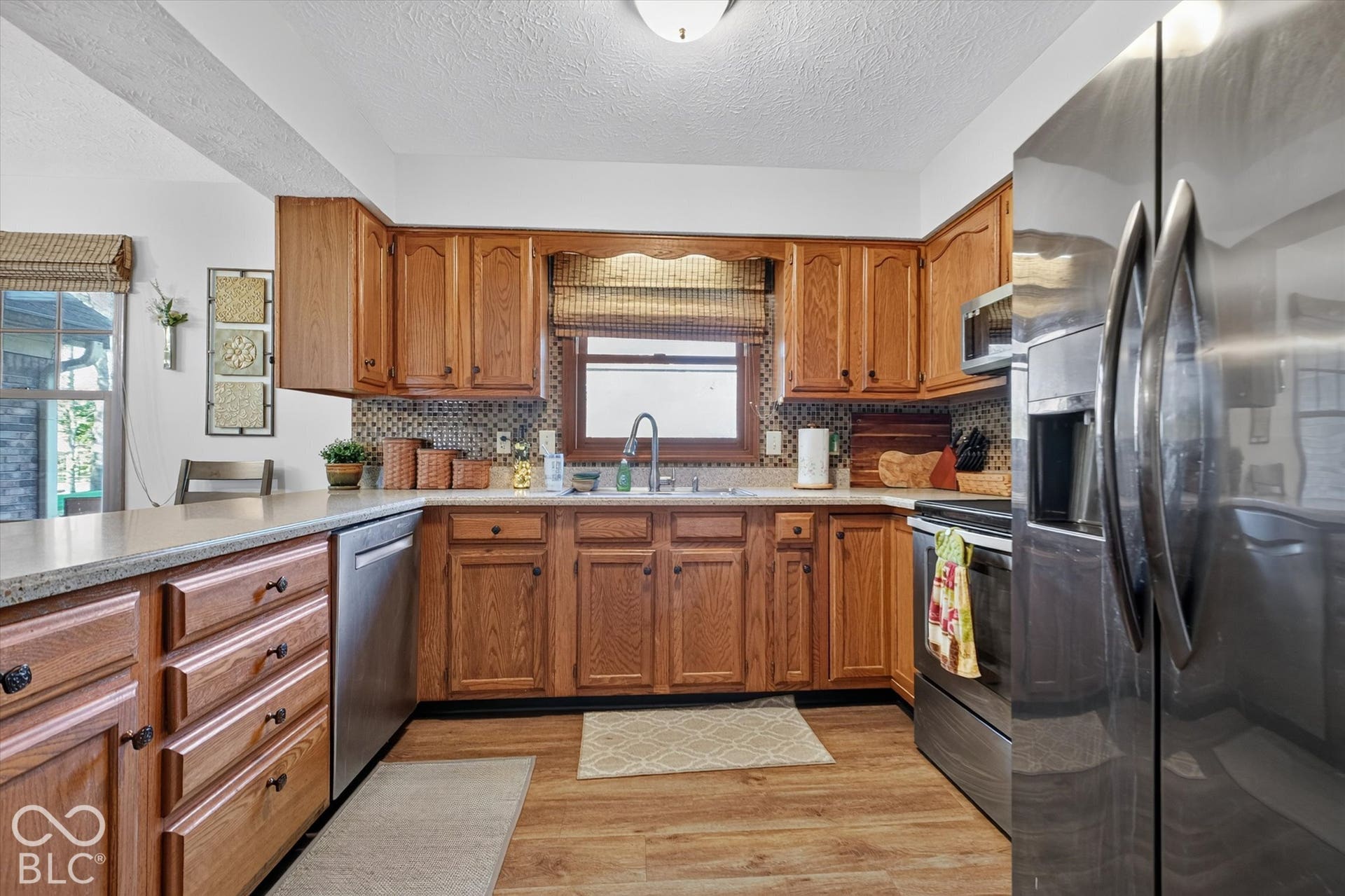 Wood-finish flooring, wood cabinetry with black hardware, stainless steel appliances, and a tiled backsplash
