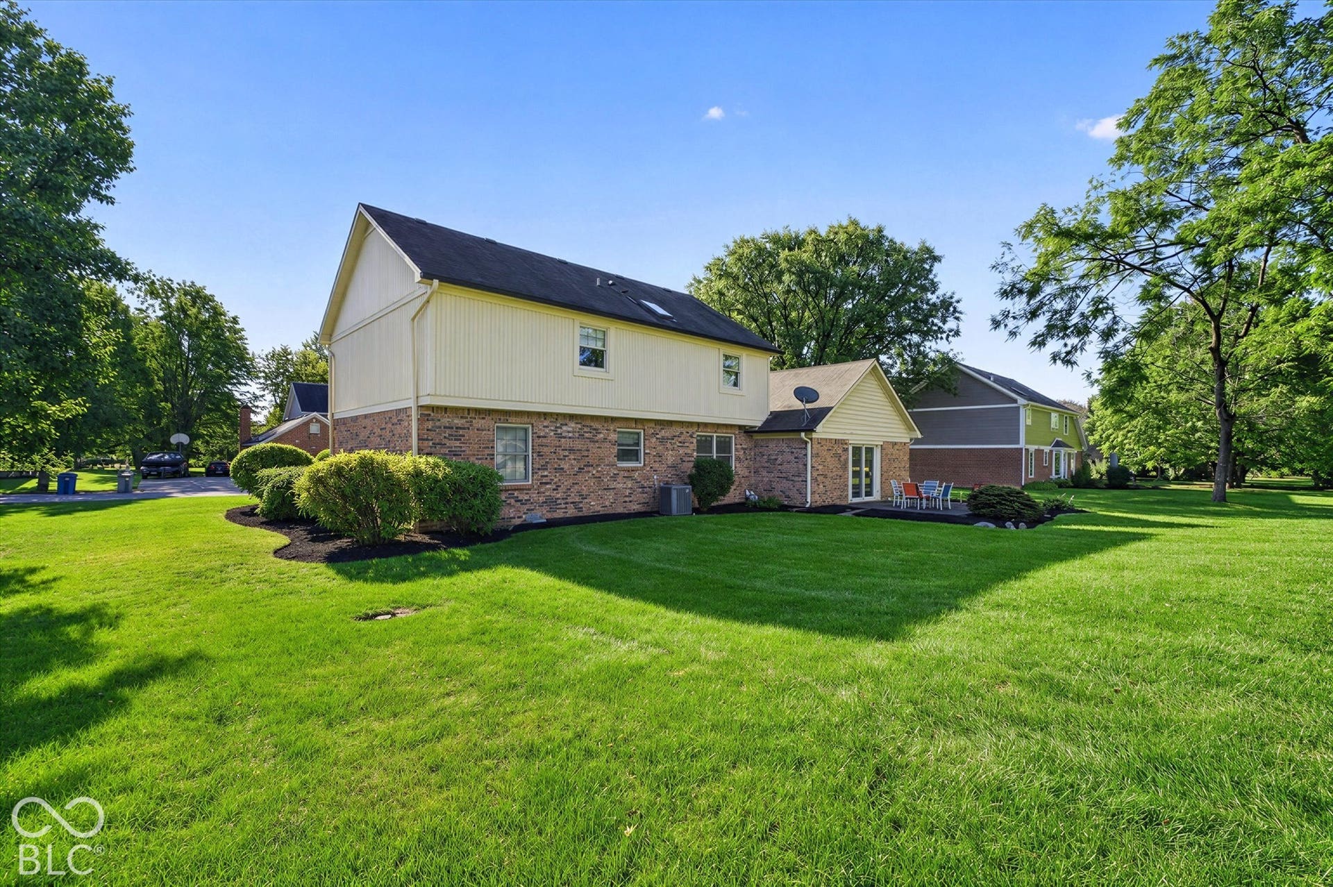 Charming brick and siding exterior with a dark roof, situated on expansive manicured grounds featuring mature trees and lush lawn