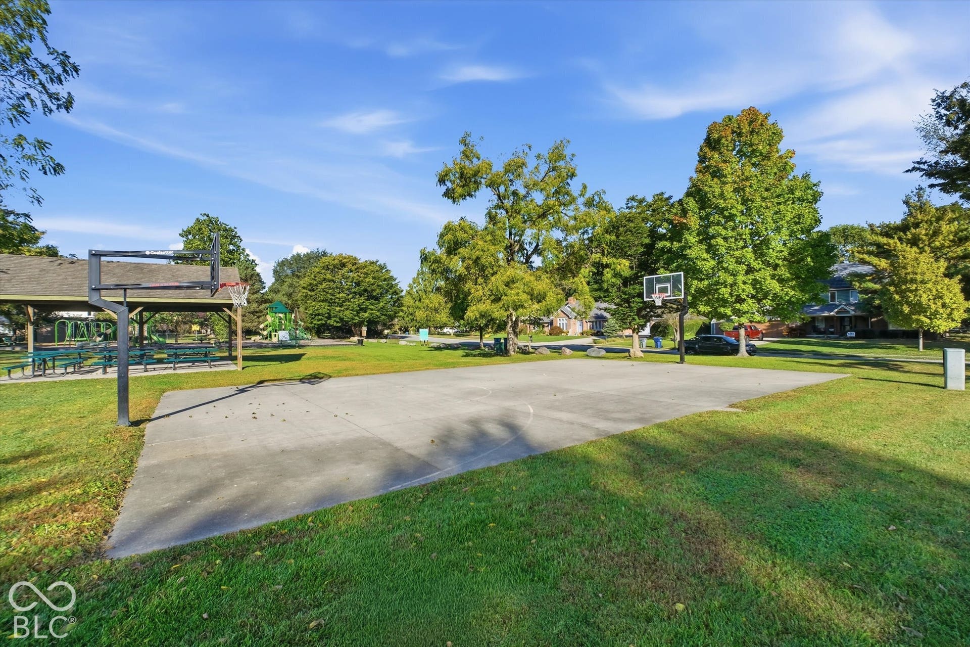 Concrete basketball court, expansive green lawn, mature trees, covered picnic area, playground structure