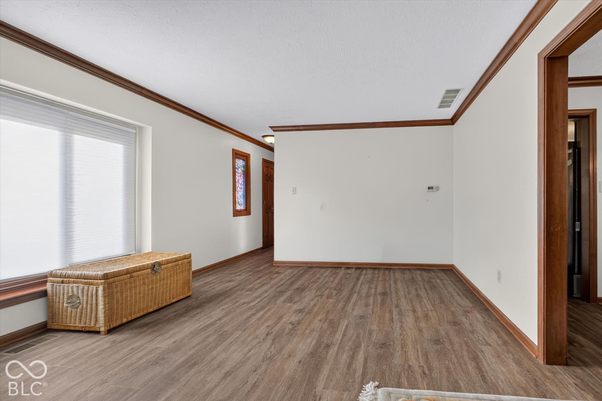Spacious room featuring wood-finish flooring, white walls, and dark wood trim