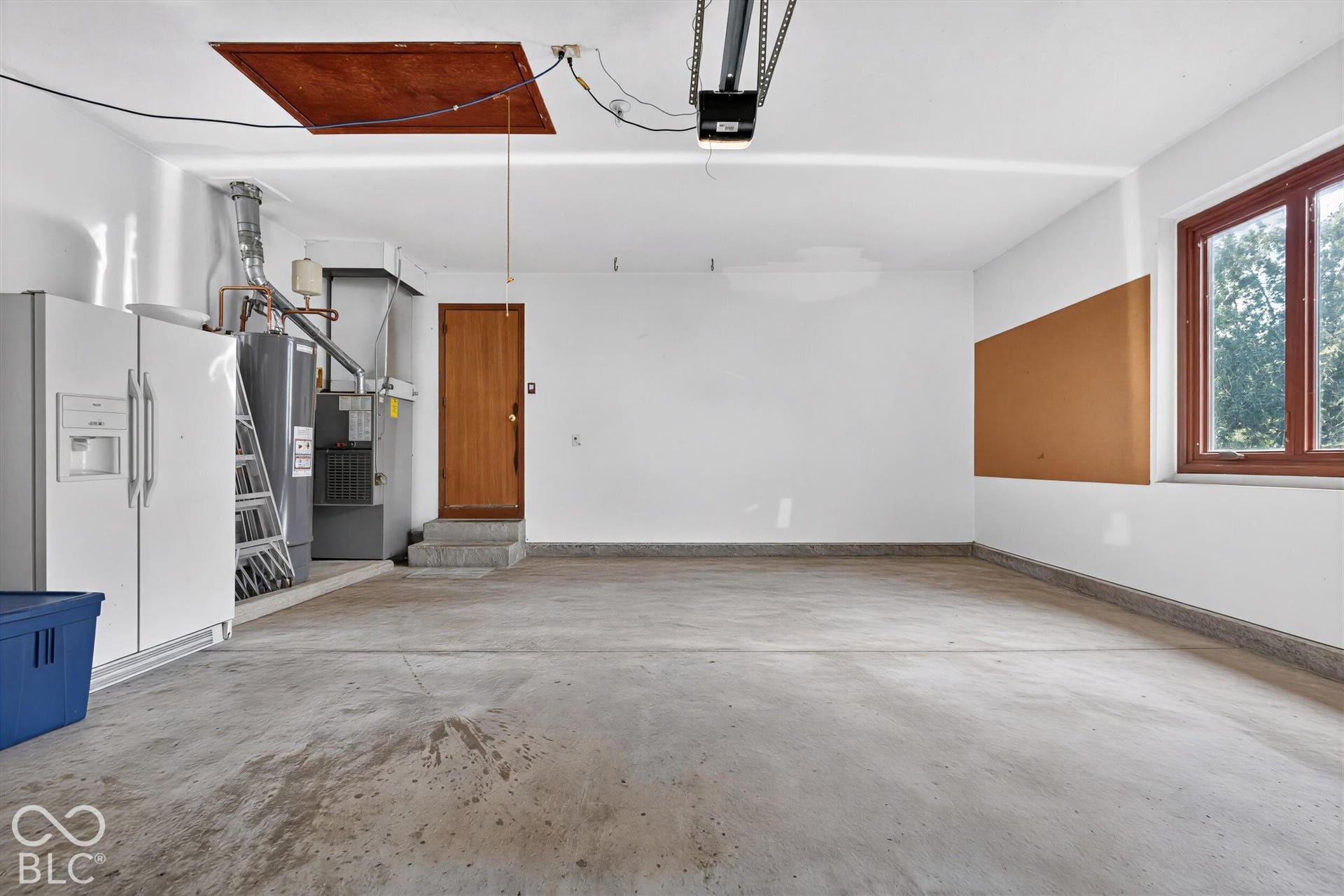 Concrete flooring with a finished white ceiling, a single window with wood-finish trim, and a built-in cork board