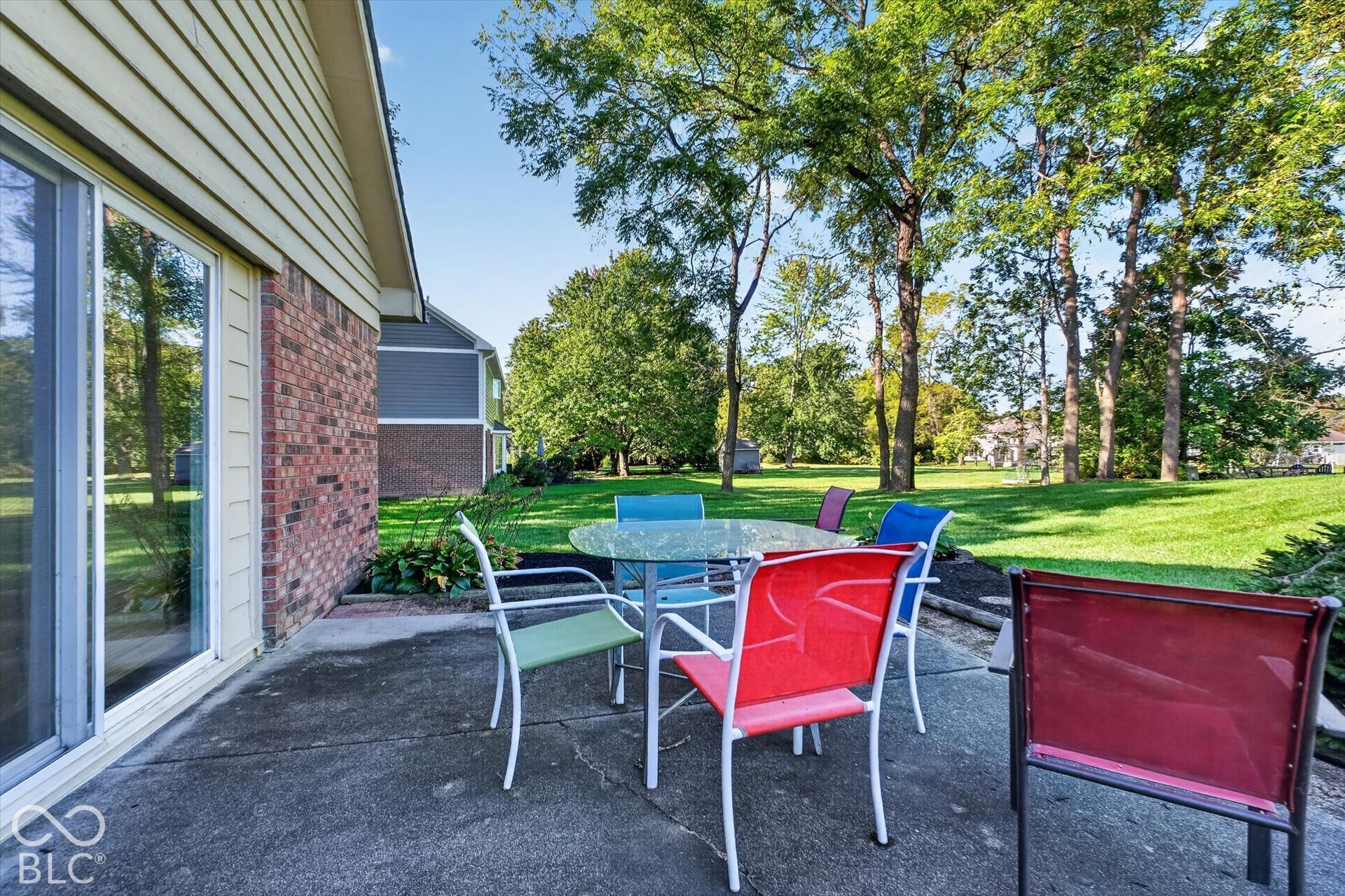 Concrete patio with a sliding glass door, brick exterior, and a spacious grassy area with mature trees