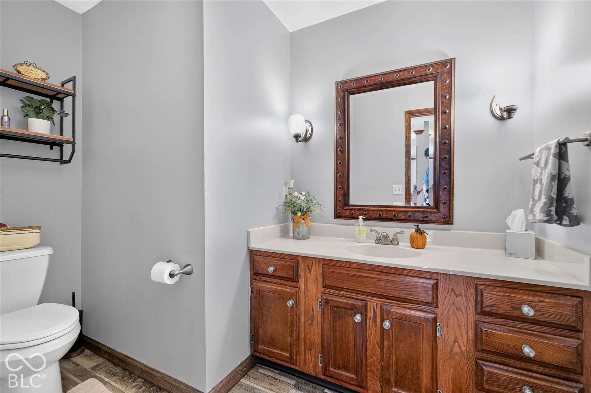 Wood-finish flooring, light gray walls, built-in wooden vanity with light countertop, framed wall mirror, and dual wall sconces
