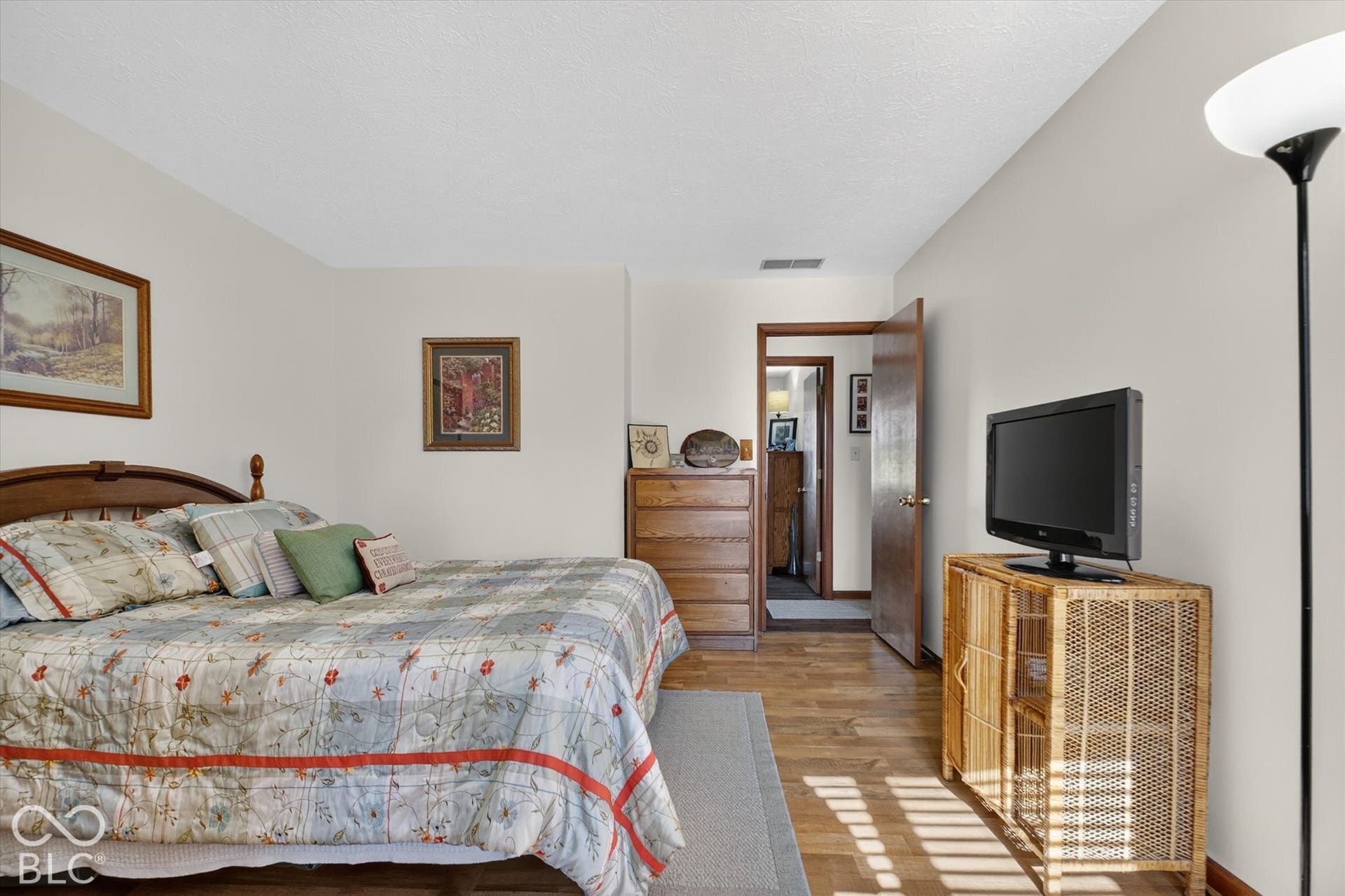 Spacious primary bedroom with hardwood flooring, abundant natural light from multiple windows, and wood-framed bed with coordinating bedding