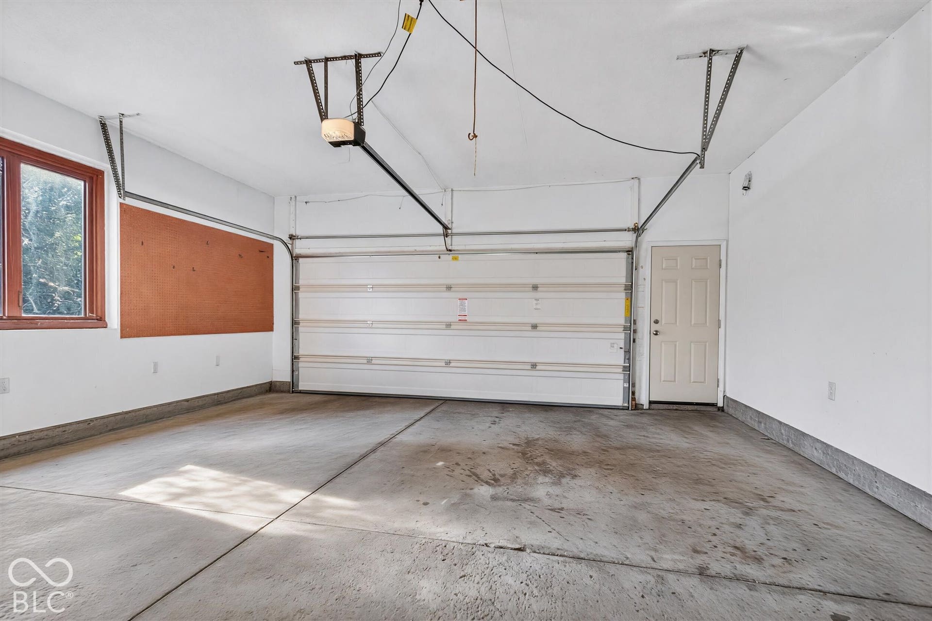 Concrete flooring, built-in cork board, single window with brown trim, overhead garage door, and a paneled interior door