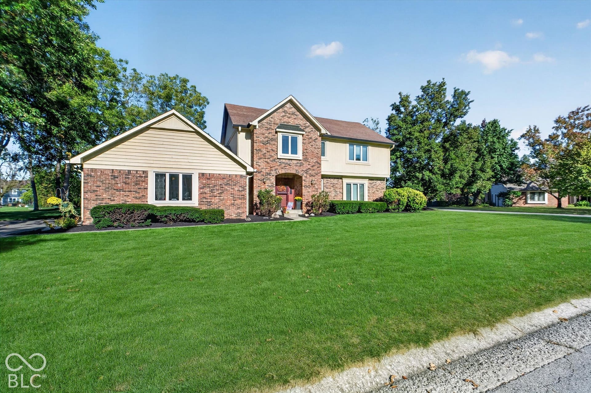 Brick and siding exterior with multiple windows, mature landscaping, and a manicured lawn