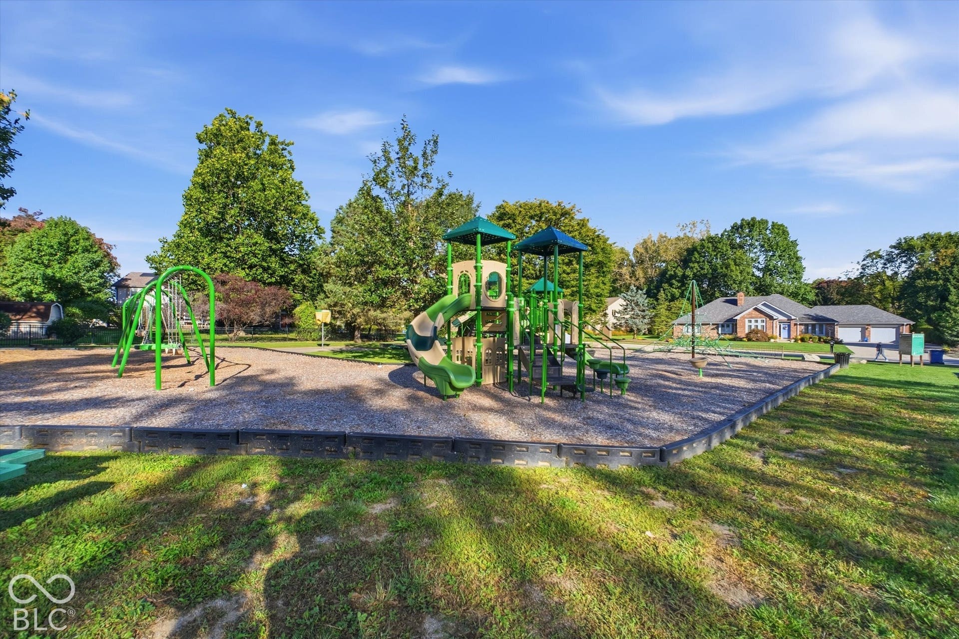 Outdoor recreation area featuring a playground structure with slides and swings, surrounded by a gravel surface