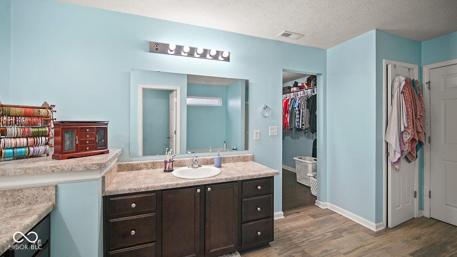 bathroom featuring vanity, wood finished floors, a spacious closet, a textured ceiling, and visible vents