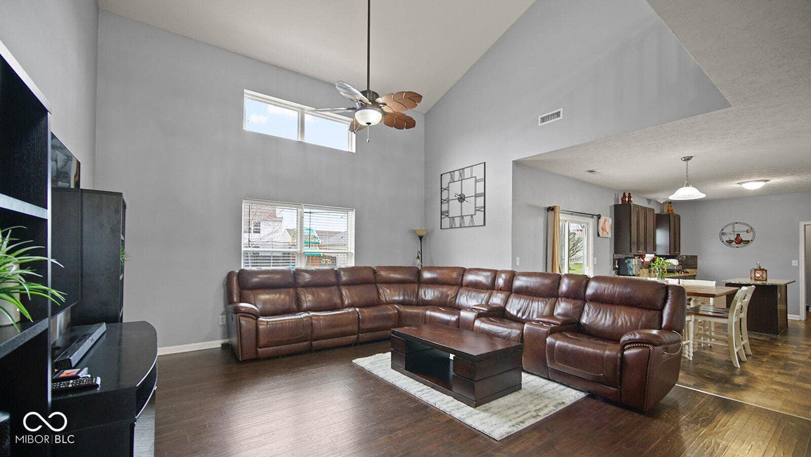 living area with visible vents, baseboards, a towering ceiling, wood finished floors, and a ceiling fan