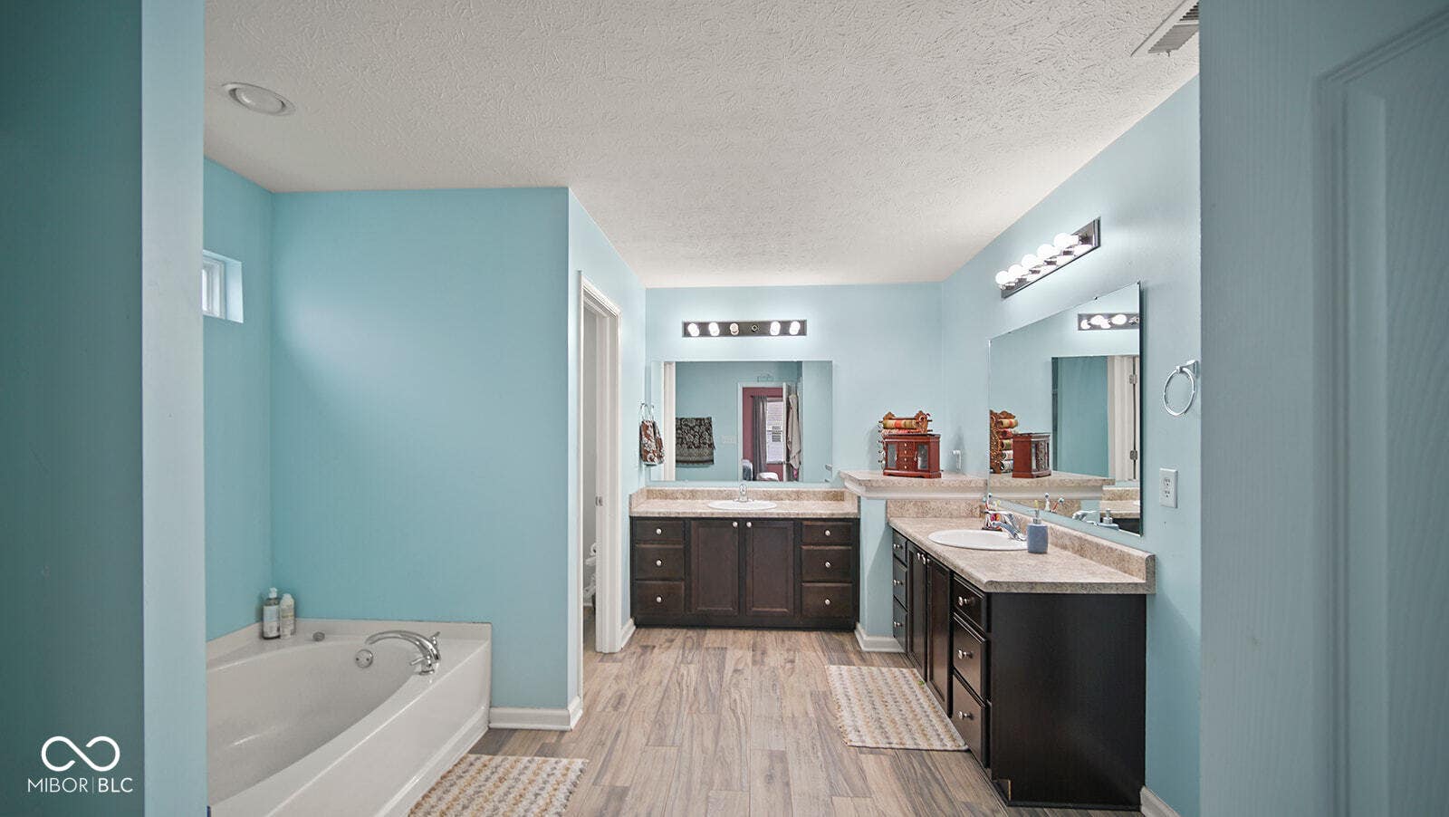full bathroom featuring a bath, a textured ceiling, wood finished floors, two vanities, and a sink