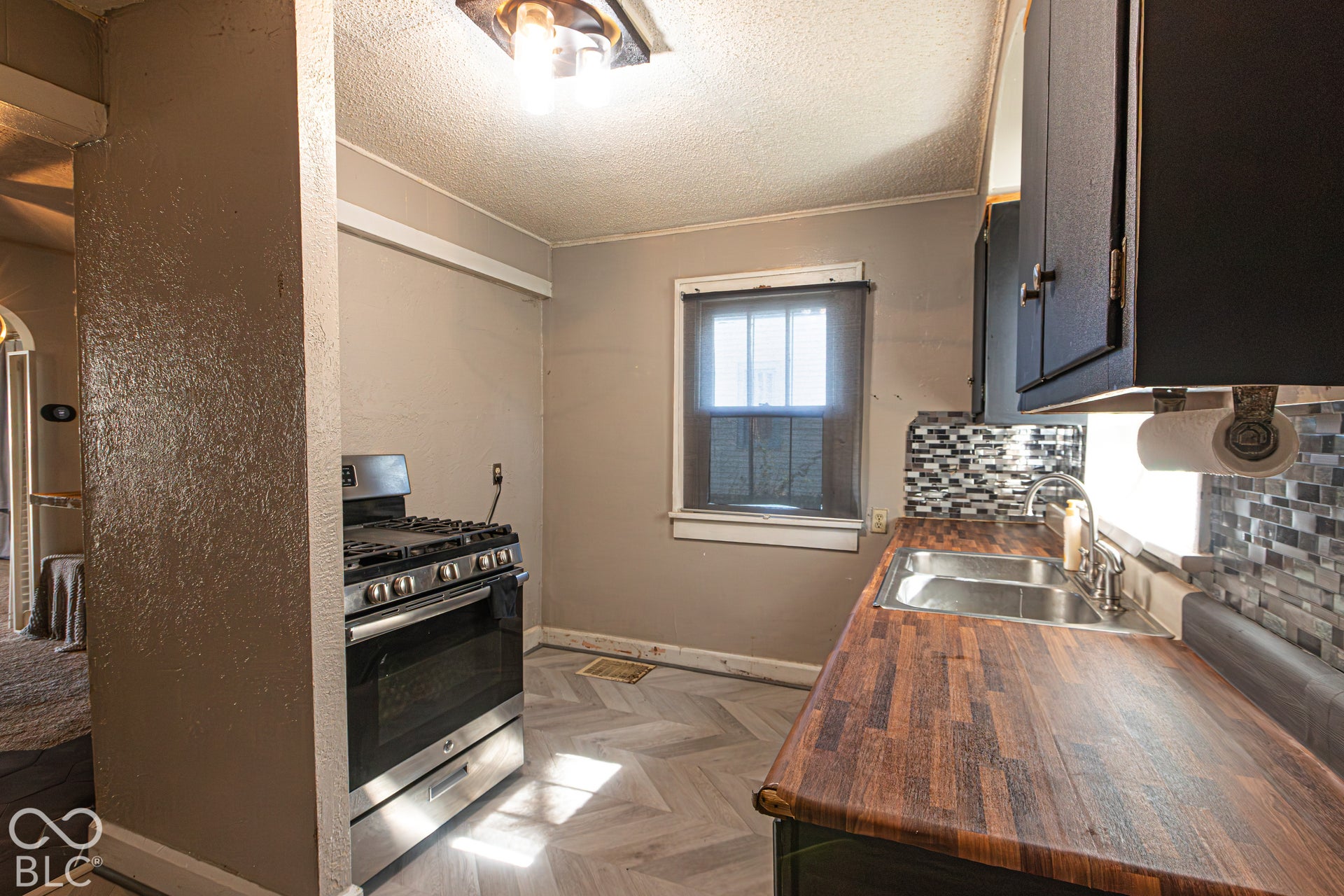 Kitchen featuring wood-finish countertops, stainless steel sink, mosaic tile backsplash, and light wood-finish flooring